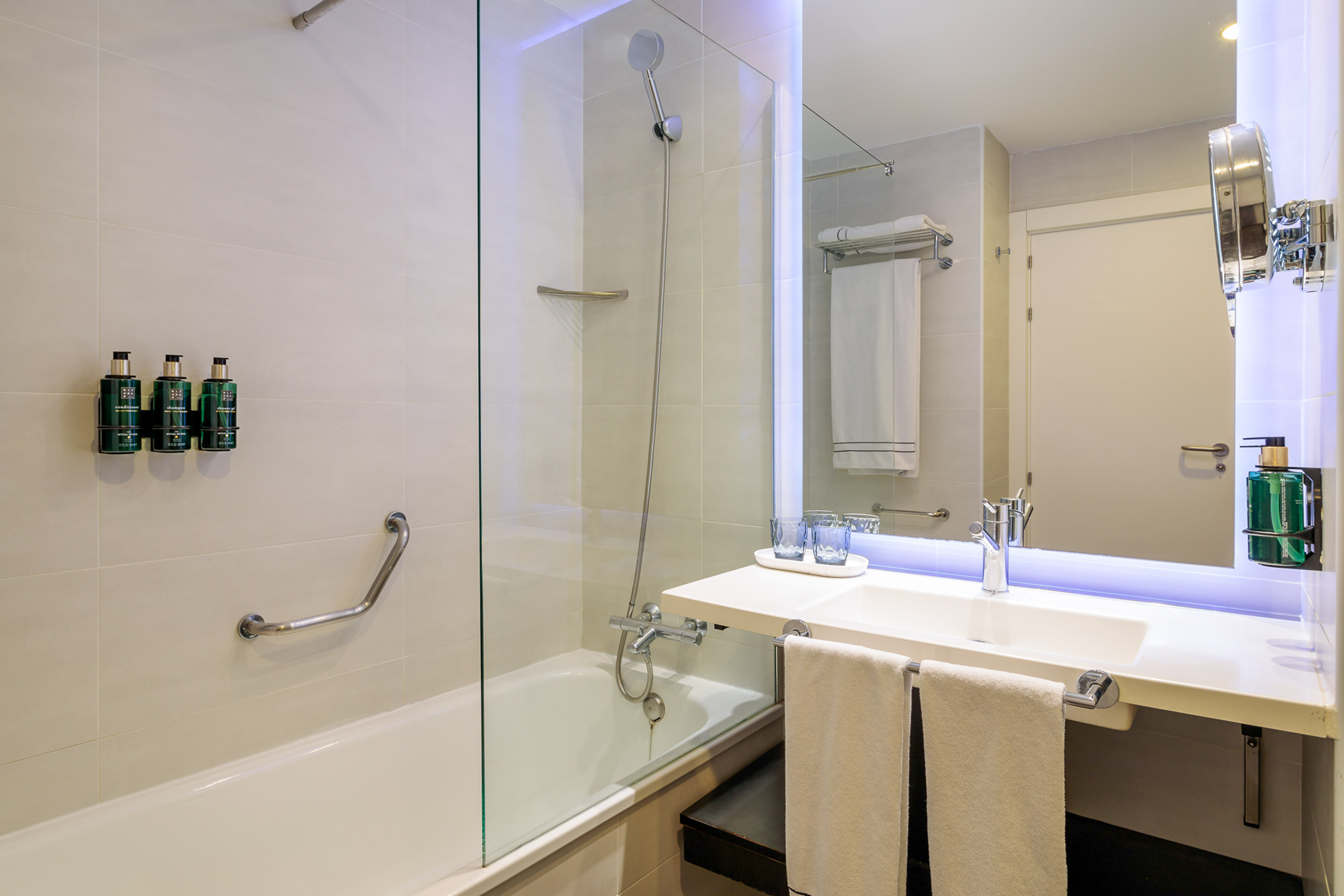 Modern hotel bathroom with bathtub, shower, vanity sink, and backlit mirror.