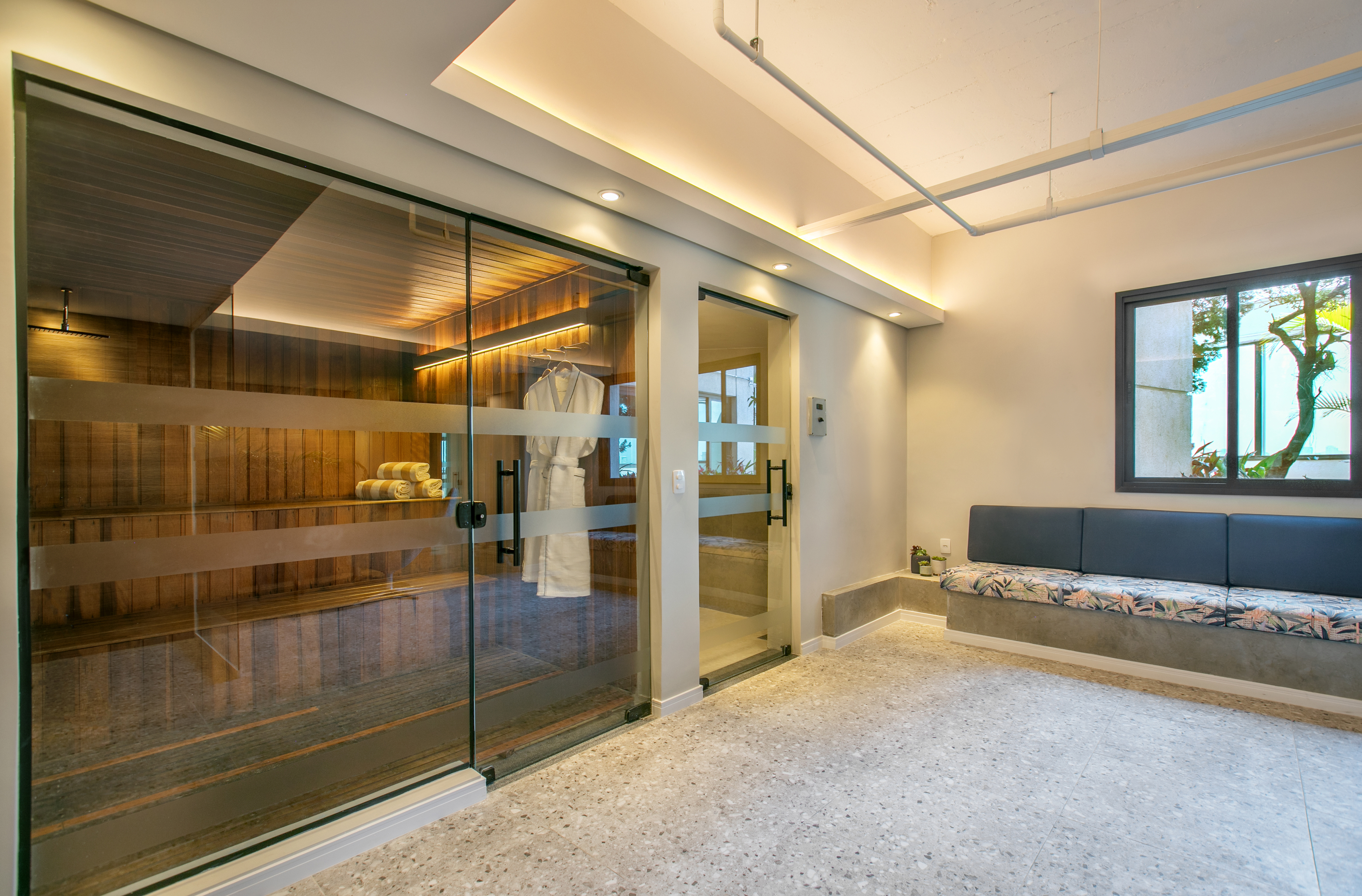 Modern spa interior with glass sauna, wooden benches, and lounge seating.