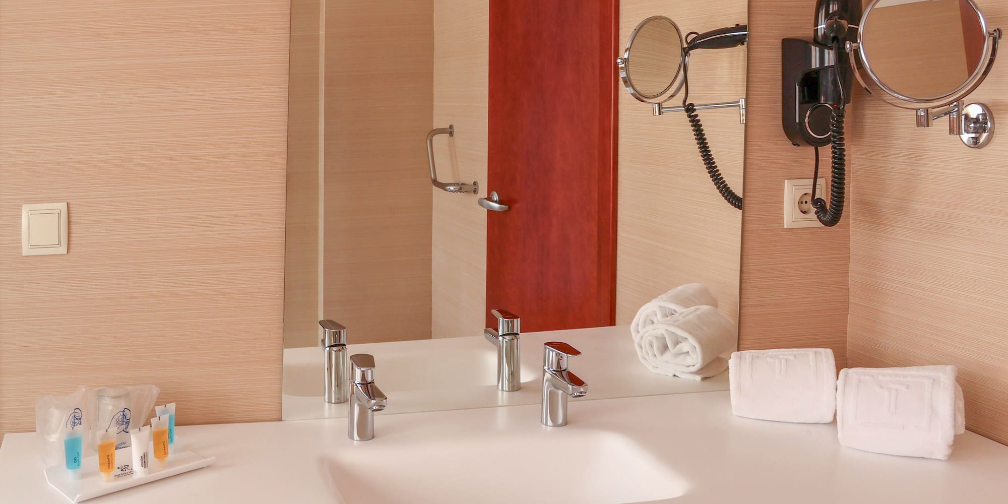 Modern hotel bathroom vanity with sink, mirror, hairdryer, and white towels.