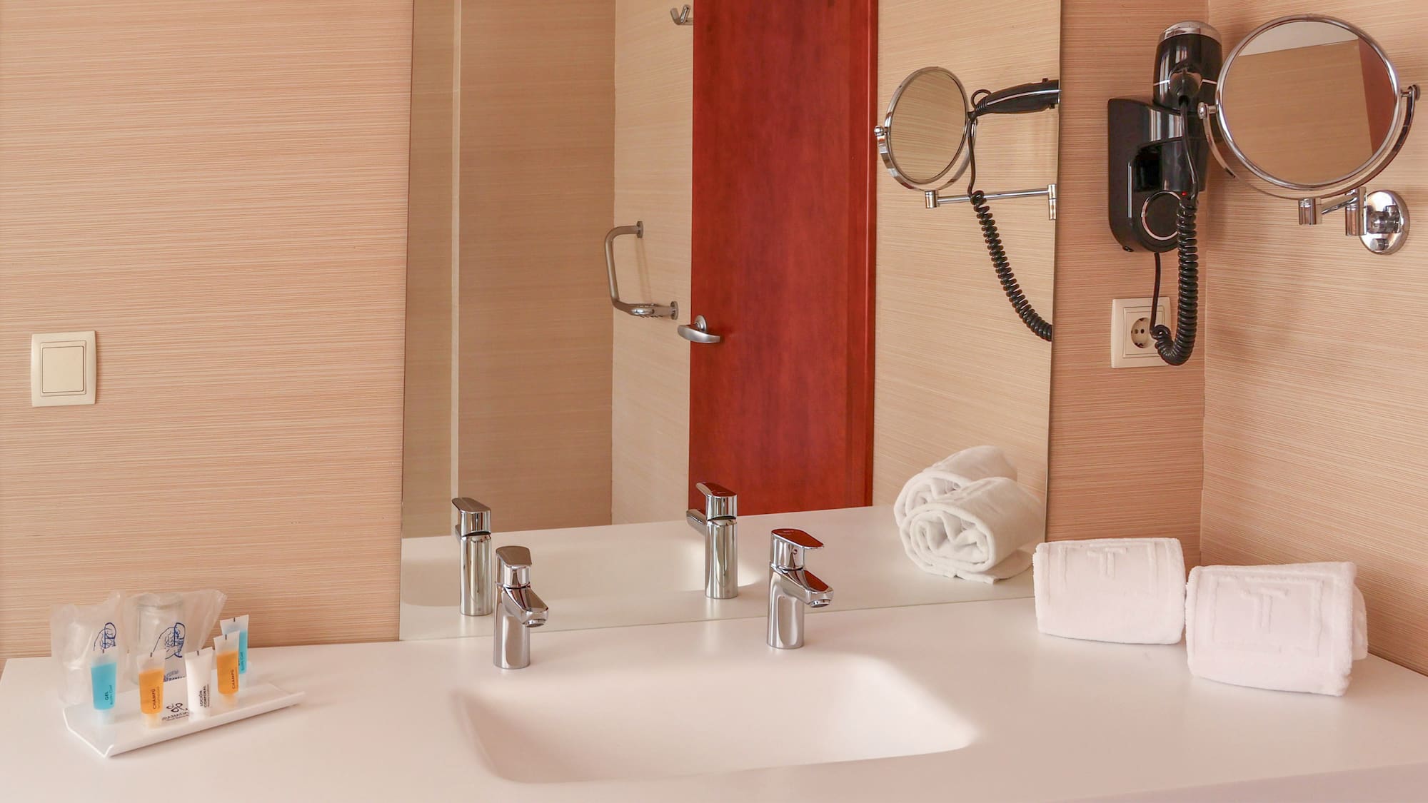 Modern hotel bathroom vanity with sink, mirror, hairdryer, and white towels.