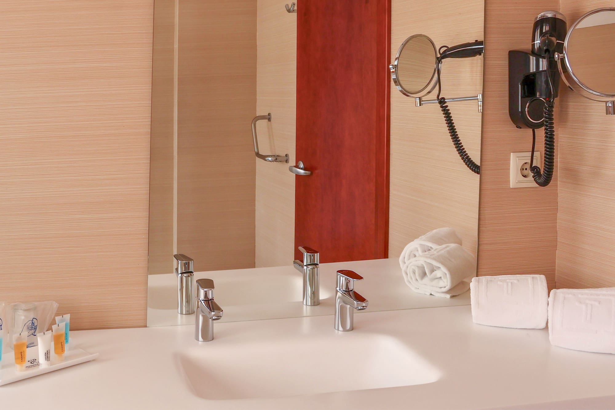 Modern hotel bathroom vanity with sink, mirror, hairdryer, and white towels.