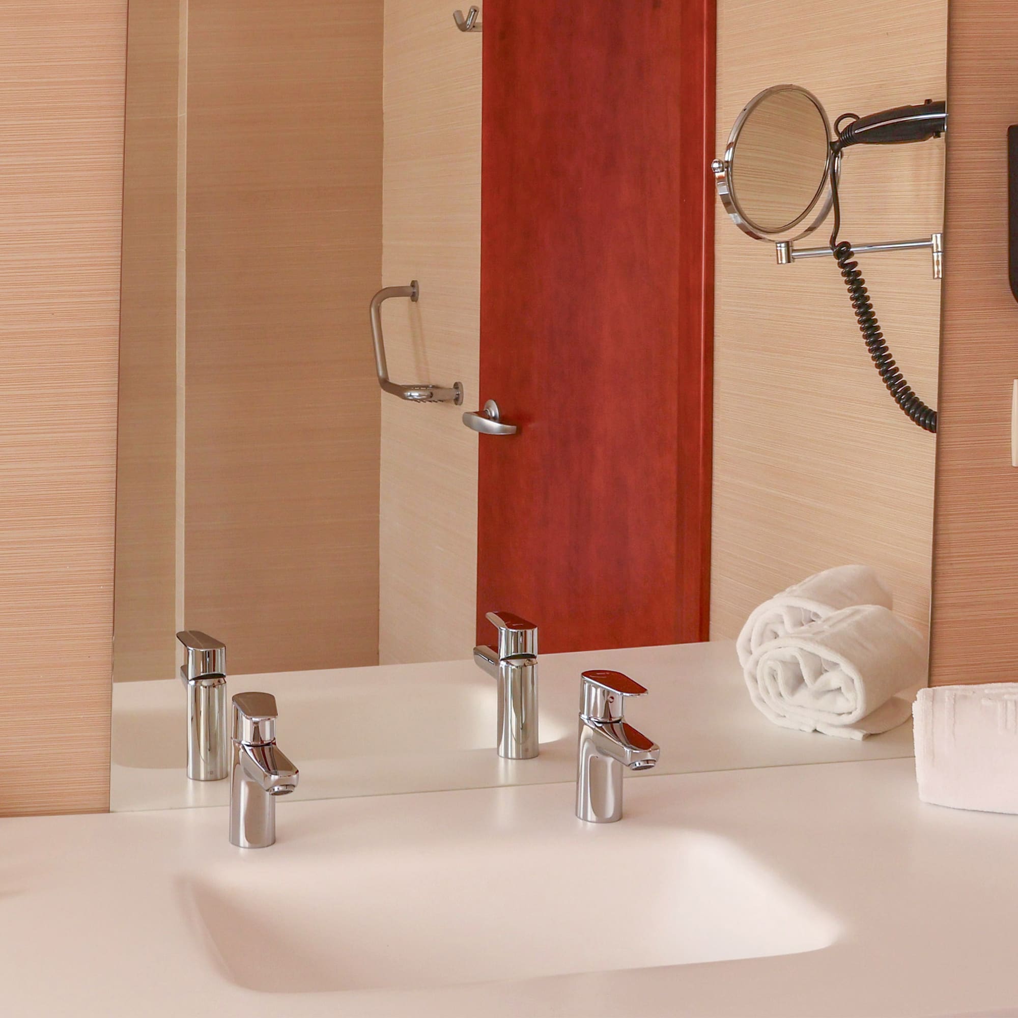 Modern hotel bathroom vanity with sink, mirror, hairdryer, and white towels.