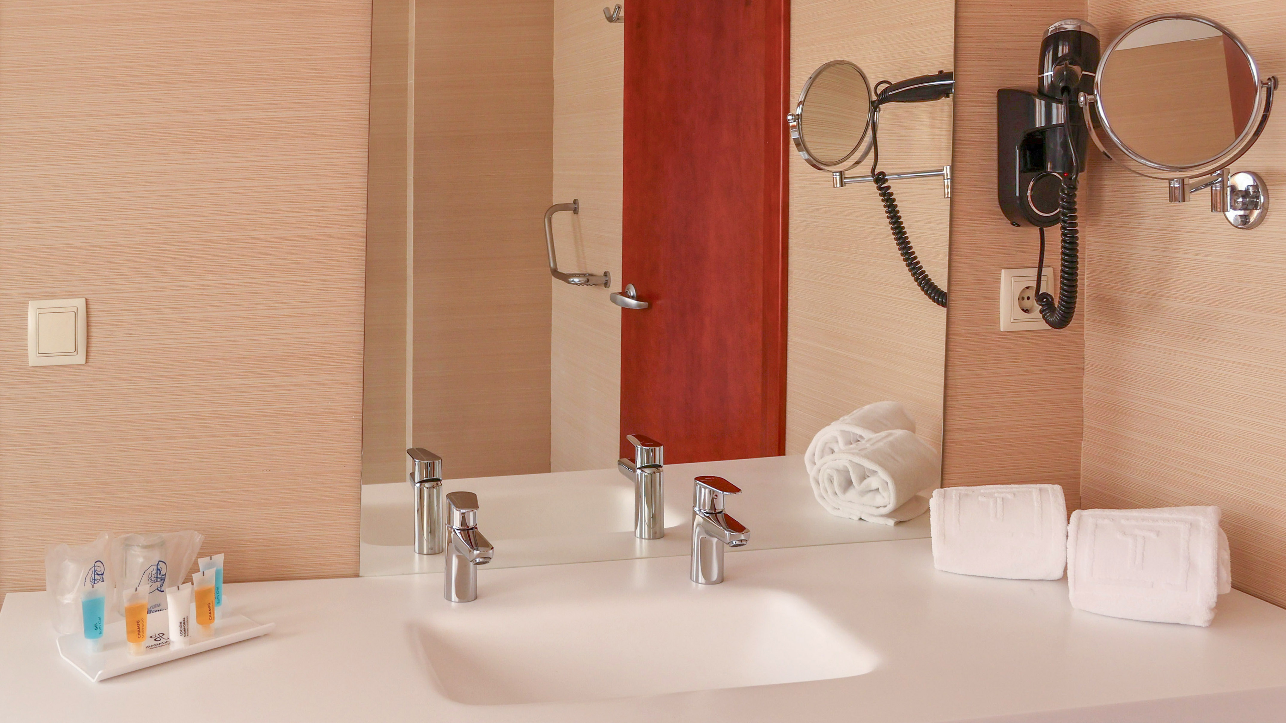 Modern hotel bathroom vanity with sink, mirror, hairdryer, and white towels.