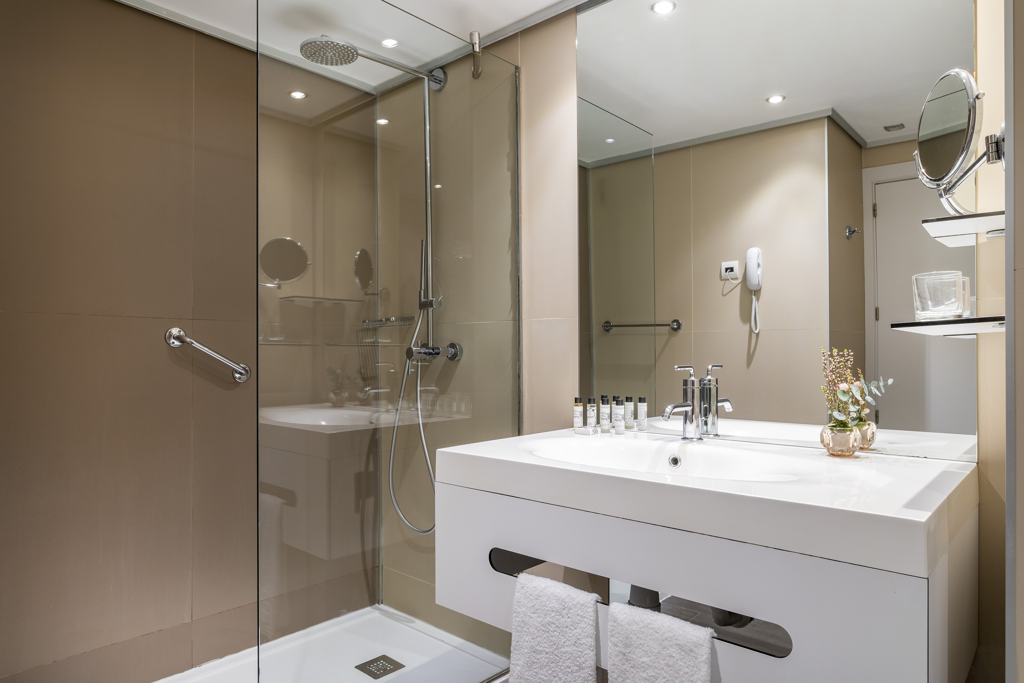 Accessible hotel bathroom: grab bar, glass shower, modern vanity with sink.