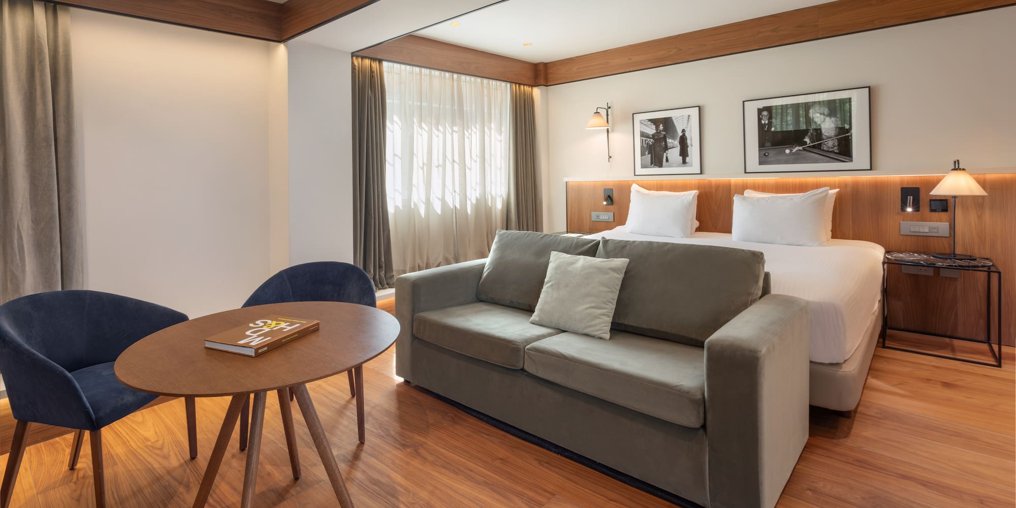 Modern hotel room with bed, grey sofa, wood floor, and seating area.