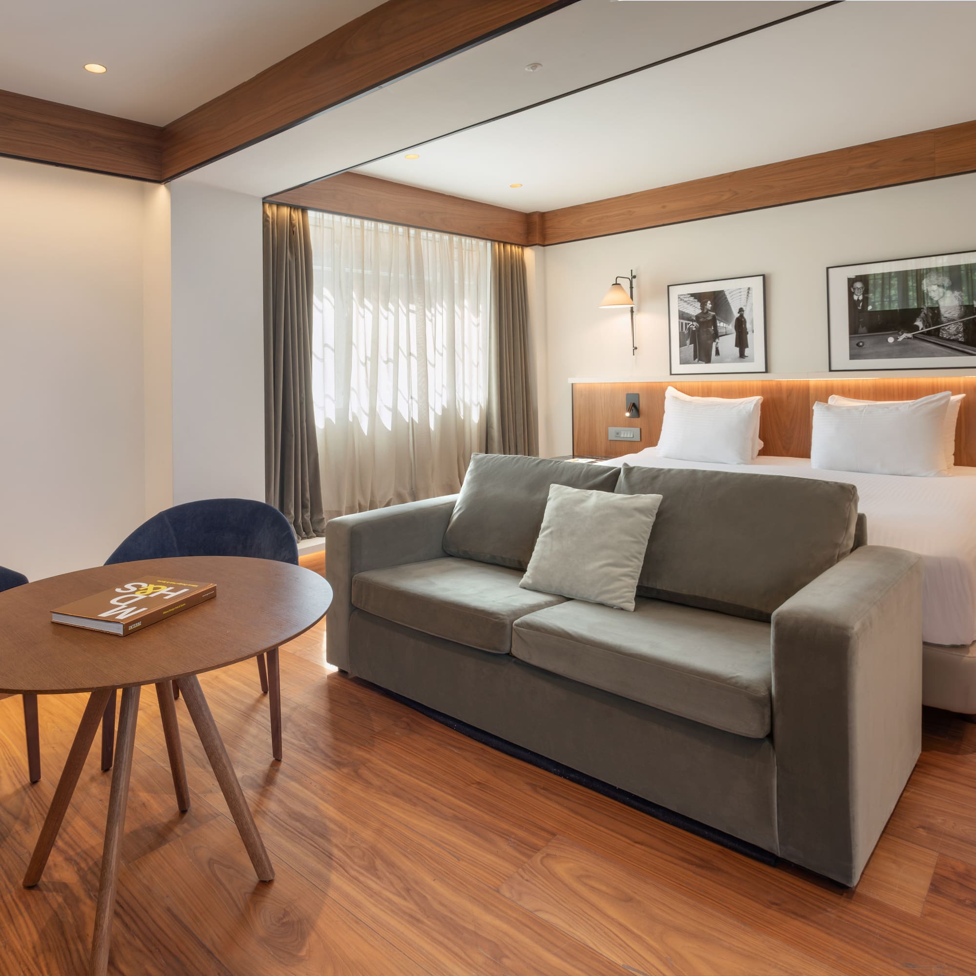 Modern hotel room with bed, grey sofa, wood floor, and seating area.