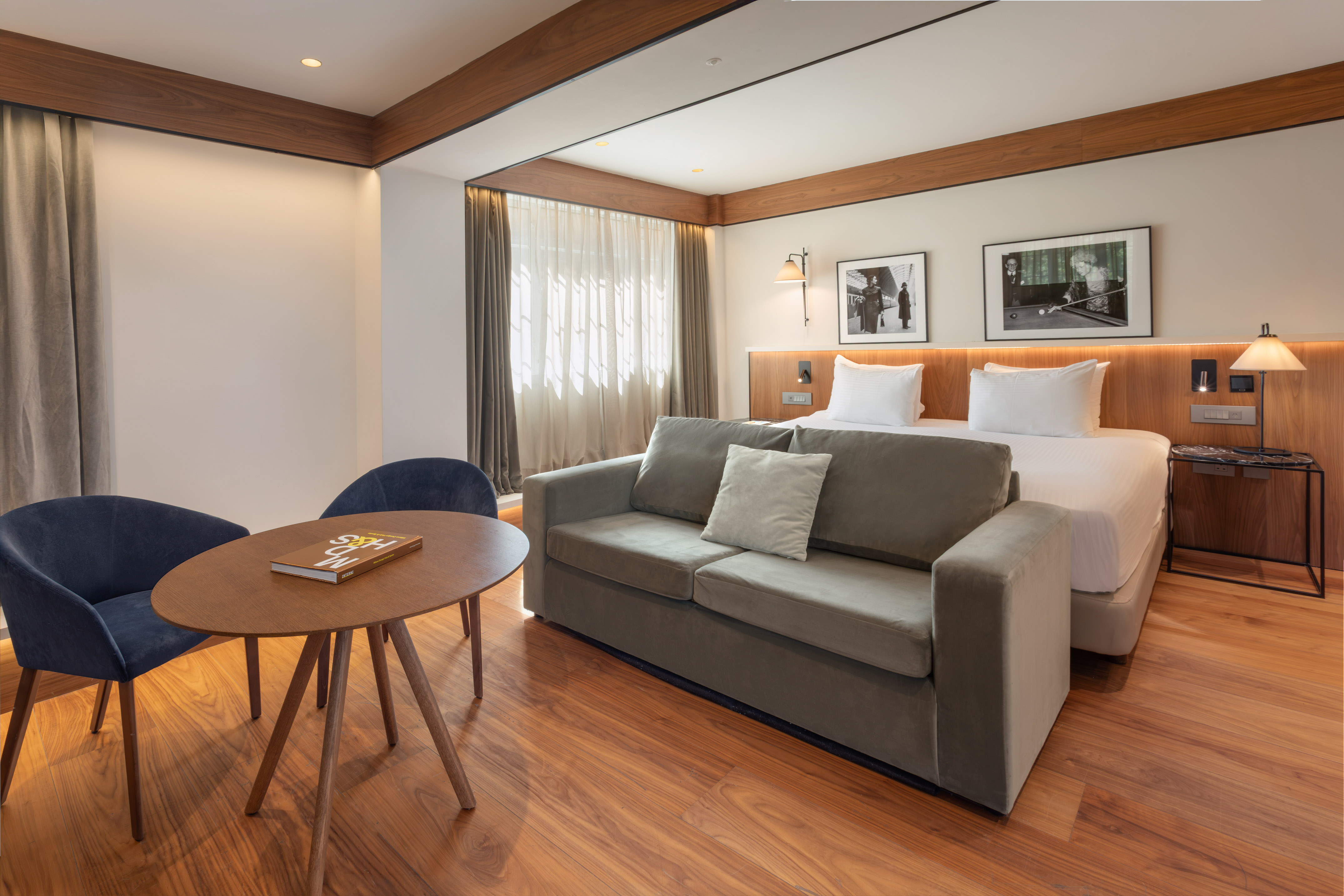 Modern hotel room with bed, grey sofa, wood floor, and seating area.
