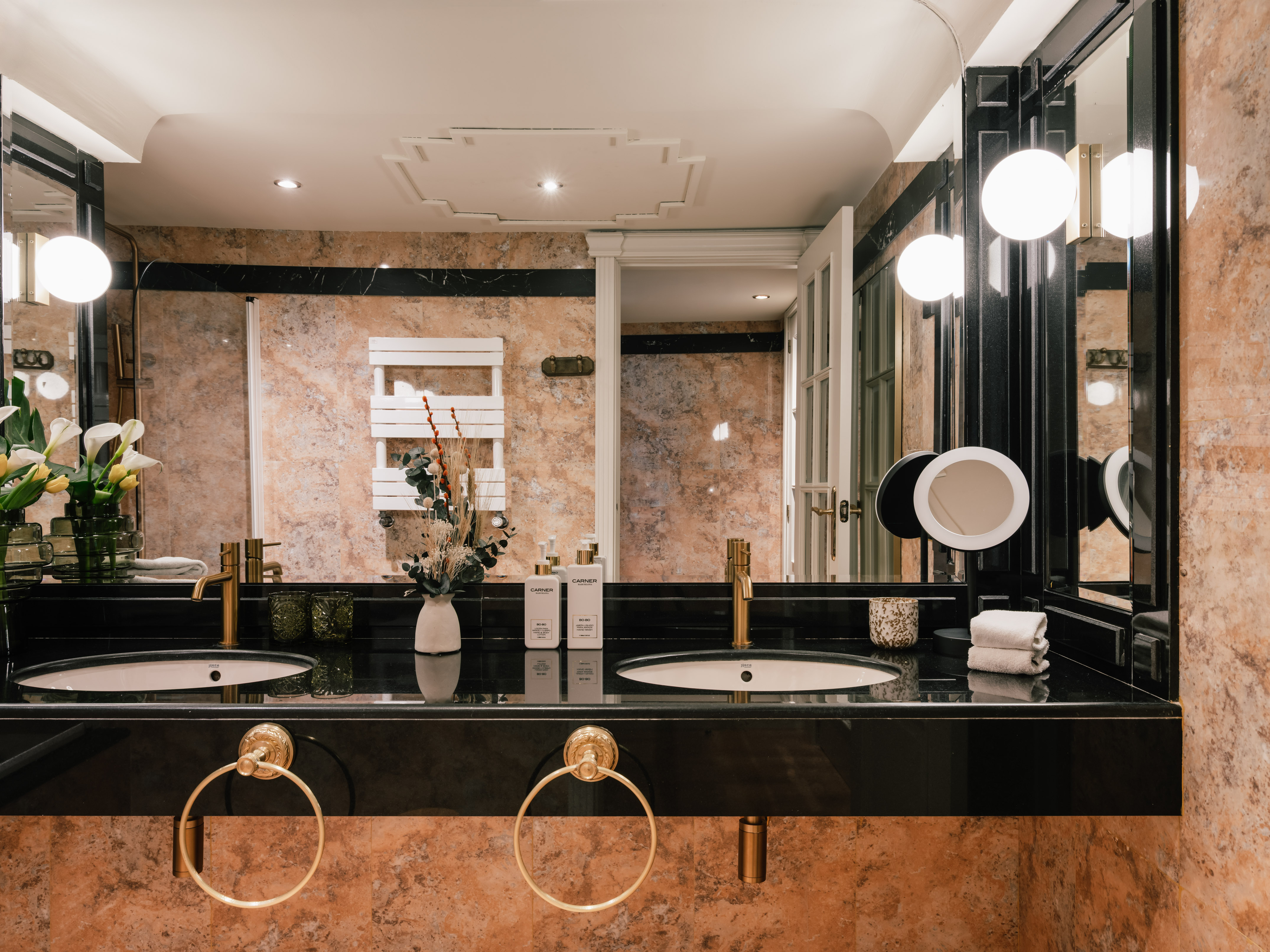 Elegant double vanity bathroom with black sinks, gold faucets, and marble walls.