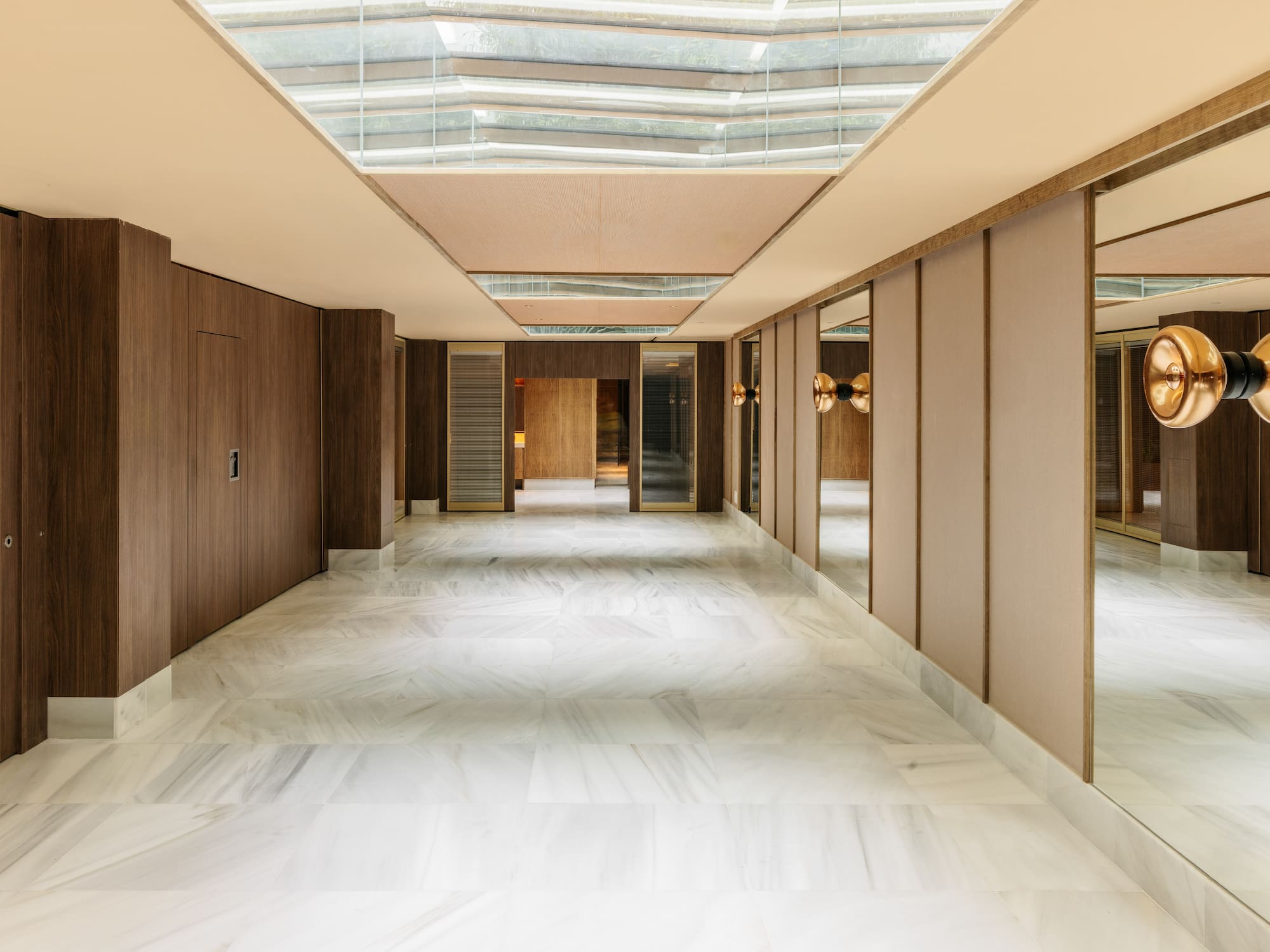Modern luxury hallway with marble floor, wood panels, mirrors, and skylight.