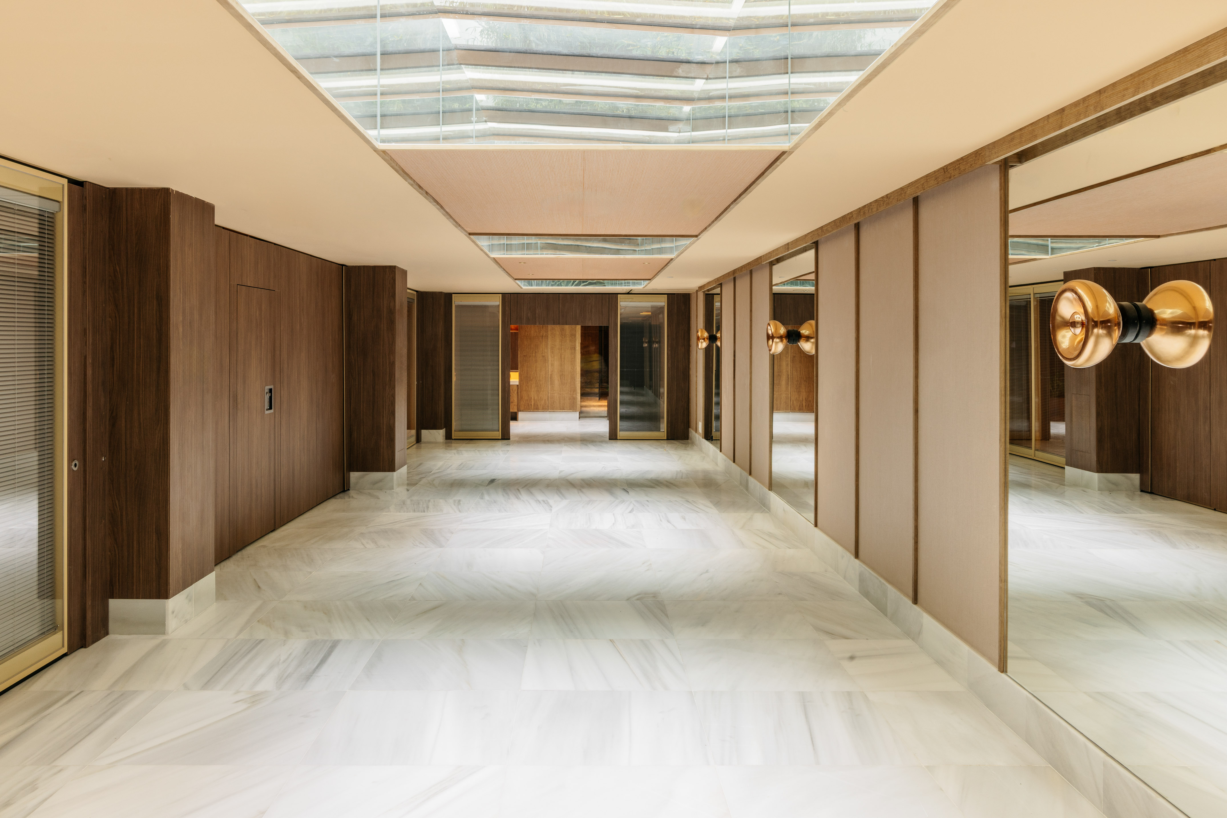 Modern luxury hallway with marble floor, wood panels, mirrors, and skylight.