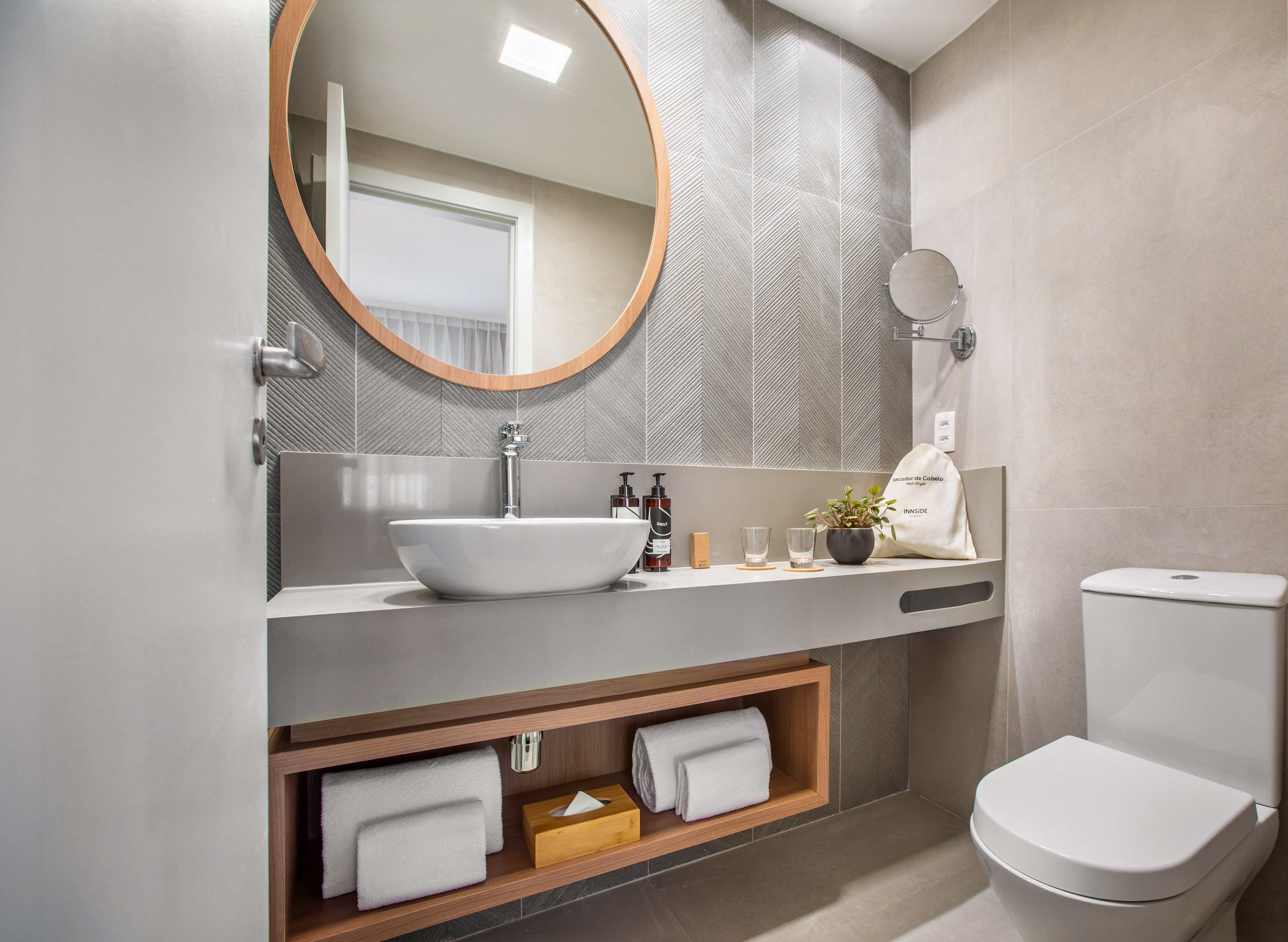 Modern hotel bathroom with round mirror, vessel sink, and toilet. Gray chevron tiles.