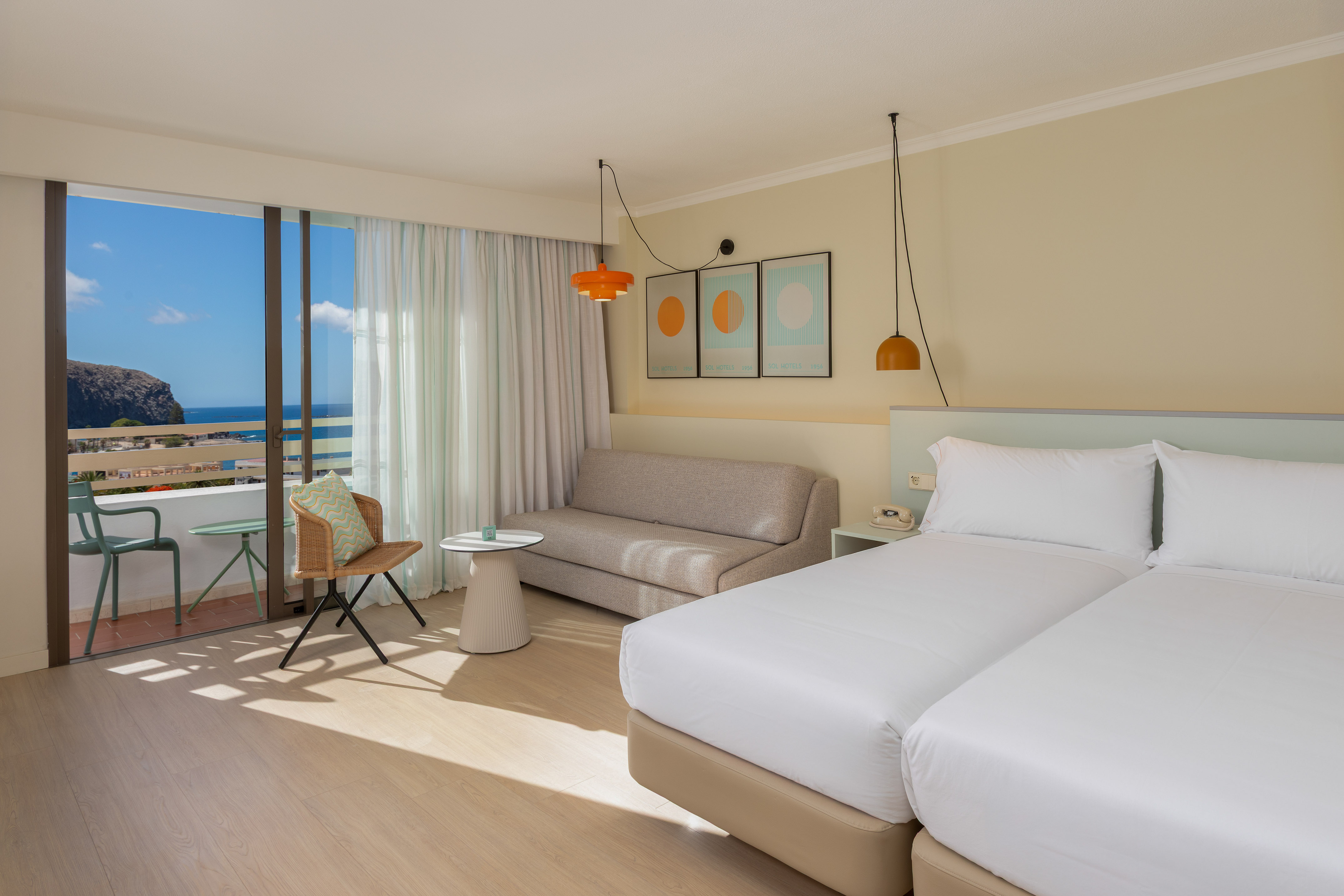 Ocean view hotel room with twin beds, sofa, and private balcony.