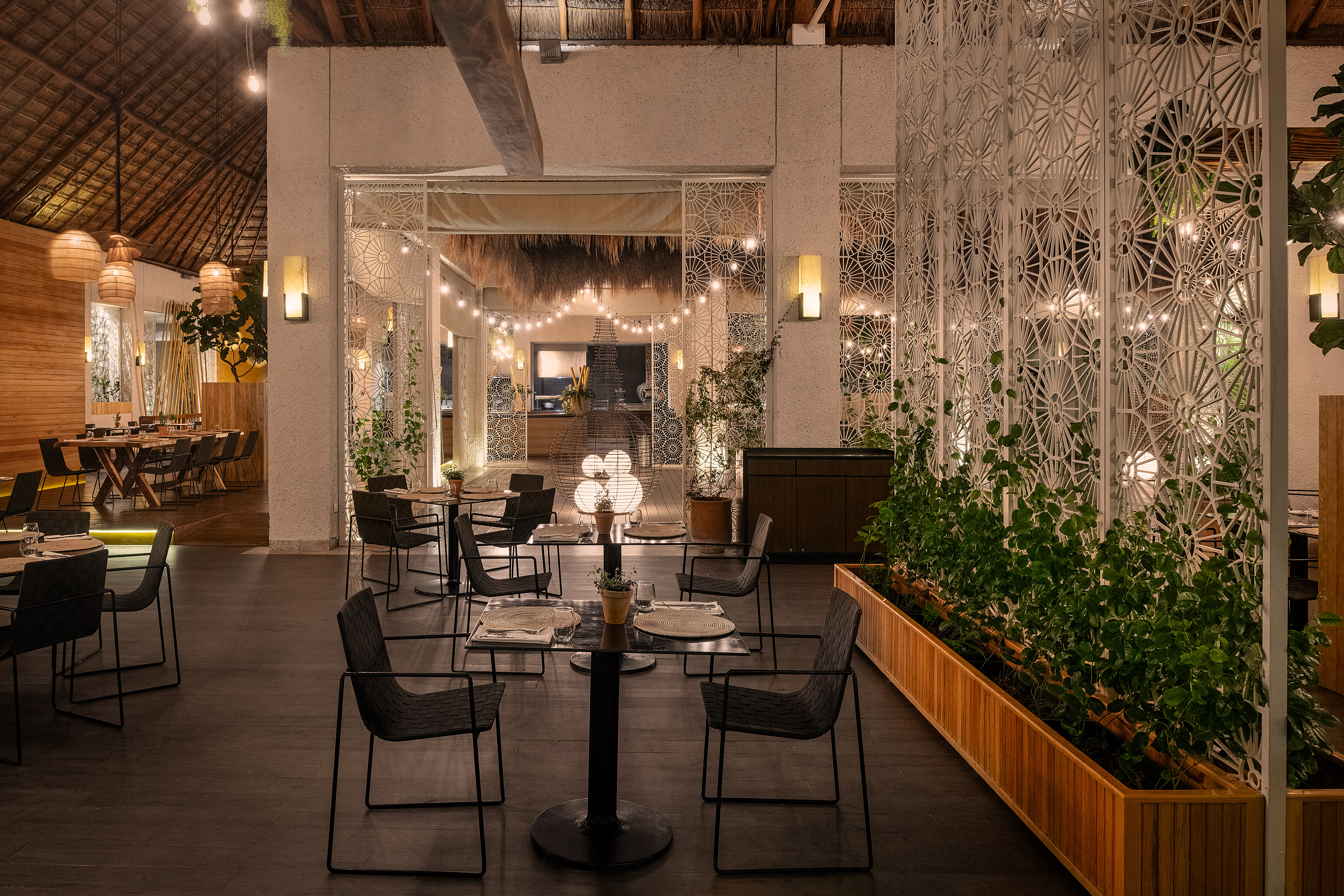 Modern restaurant interior, ornate screens, lush plants, warm lighting.