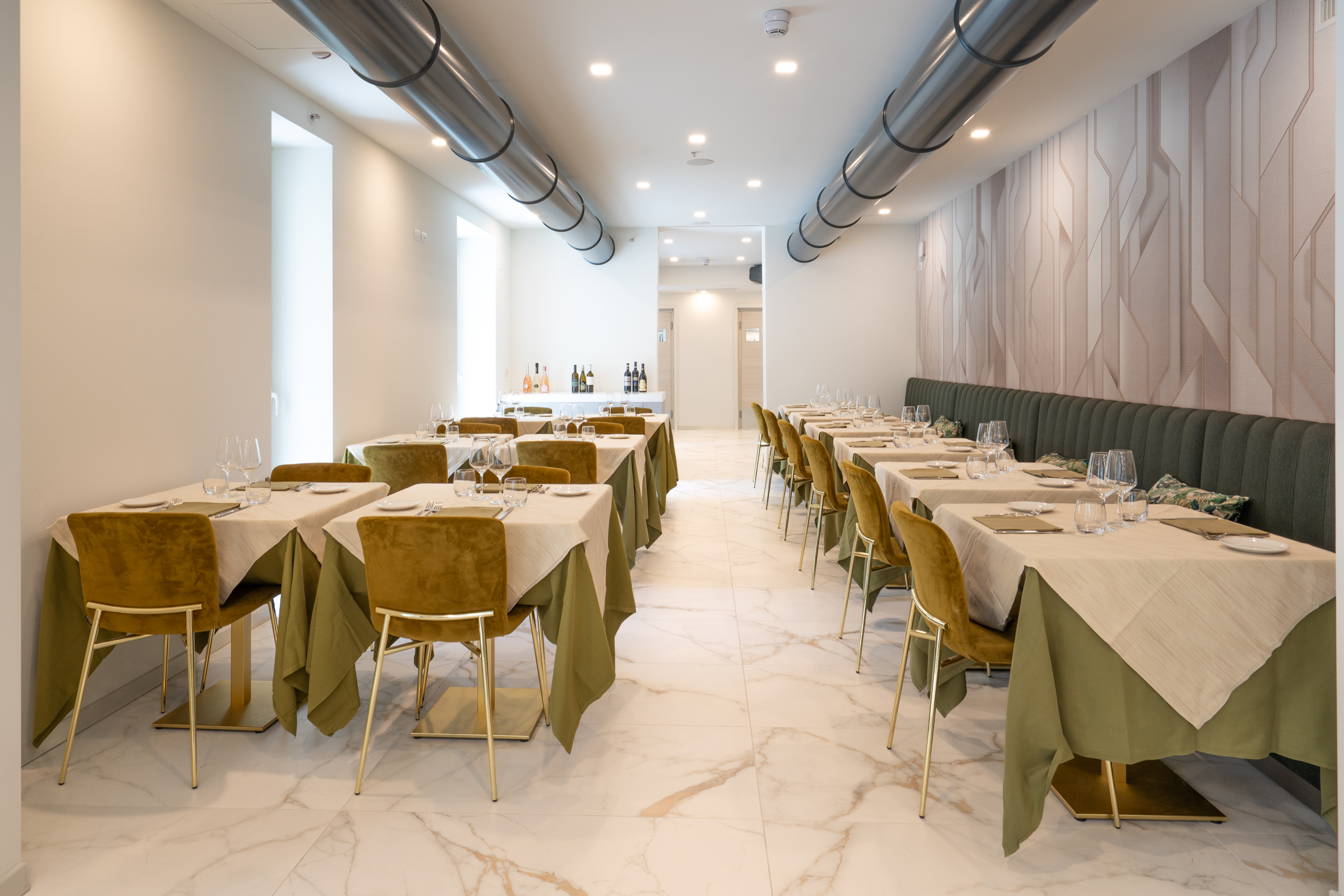 Modern restaurant with olive green seating, set tables, marble, industrial ducts.