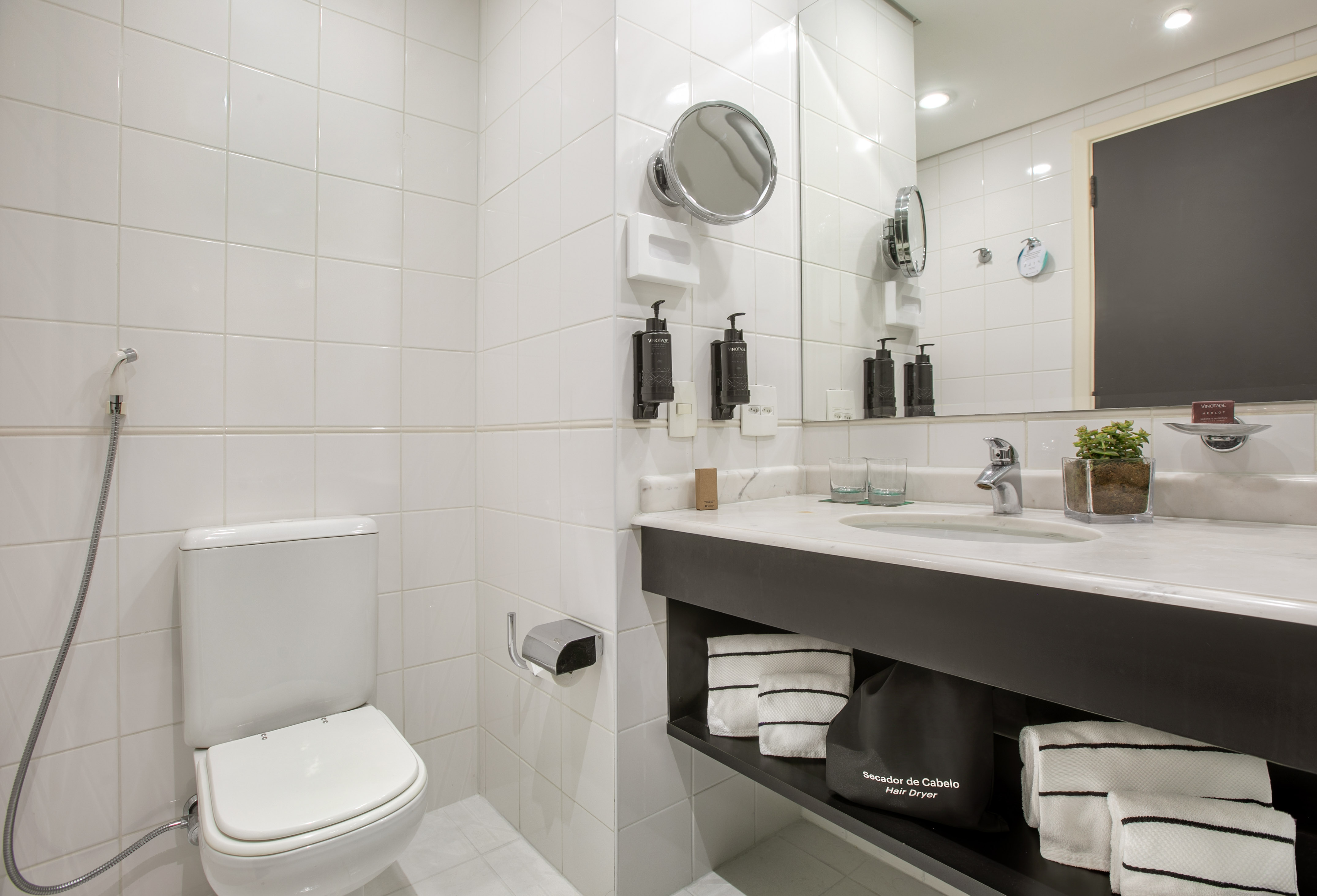 White tiled bathroom with toilet, modern vanity, mirror, and hair dryer.