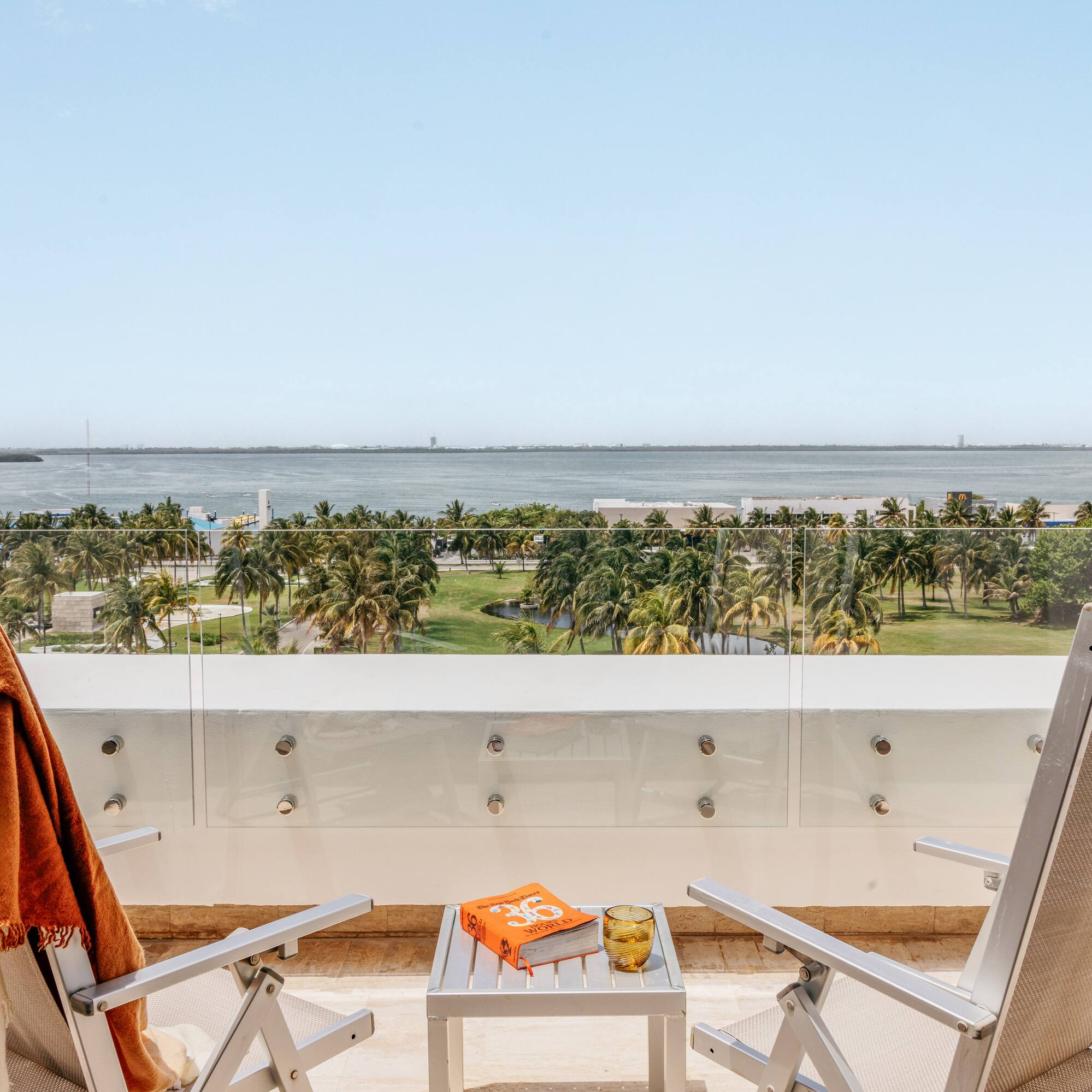 Balcony ocean view, tropical palm trees, two lounge chairs, and a book.