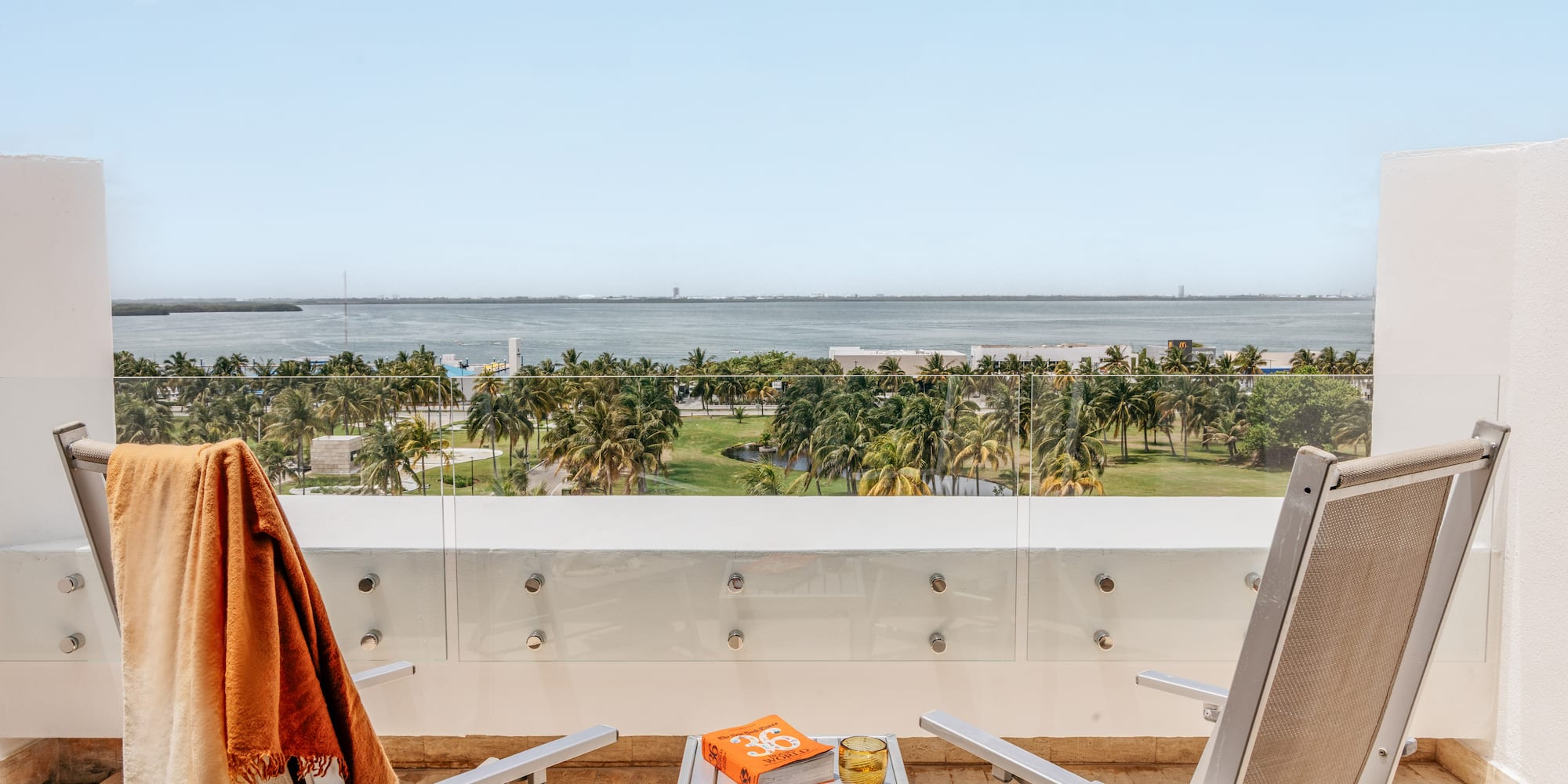 Balcony ocean view, tropical palm trees, two lounge chairs, and a book.