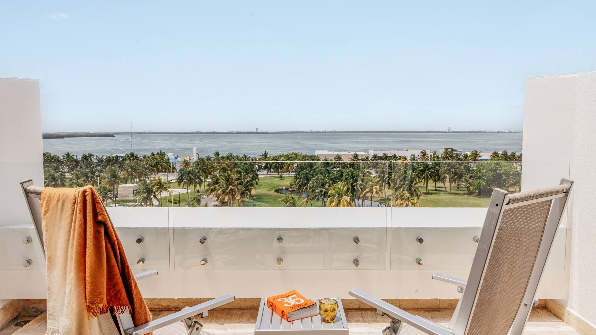 Balcony ocean view, tropical palm trees, two lounge chairs, and a book.