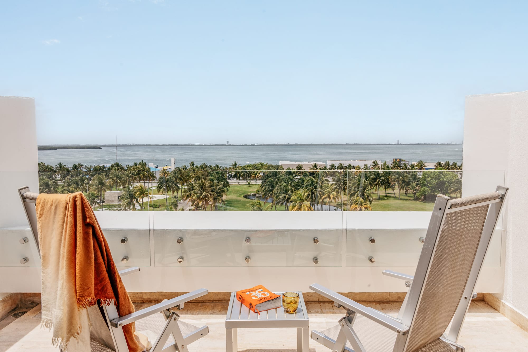 Balcony ocean view, tropical palm trees, two lounge chairs, and a book.