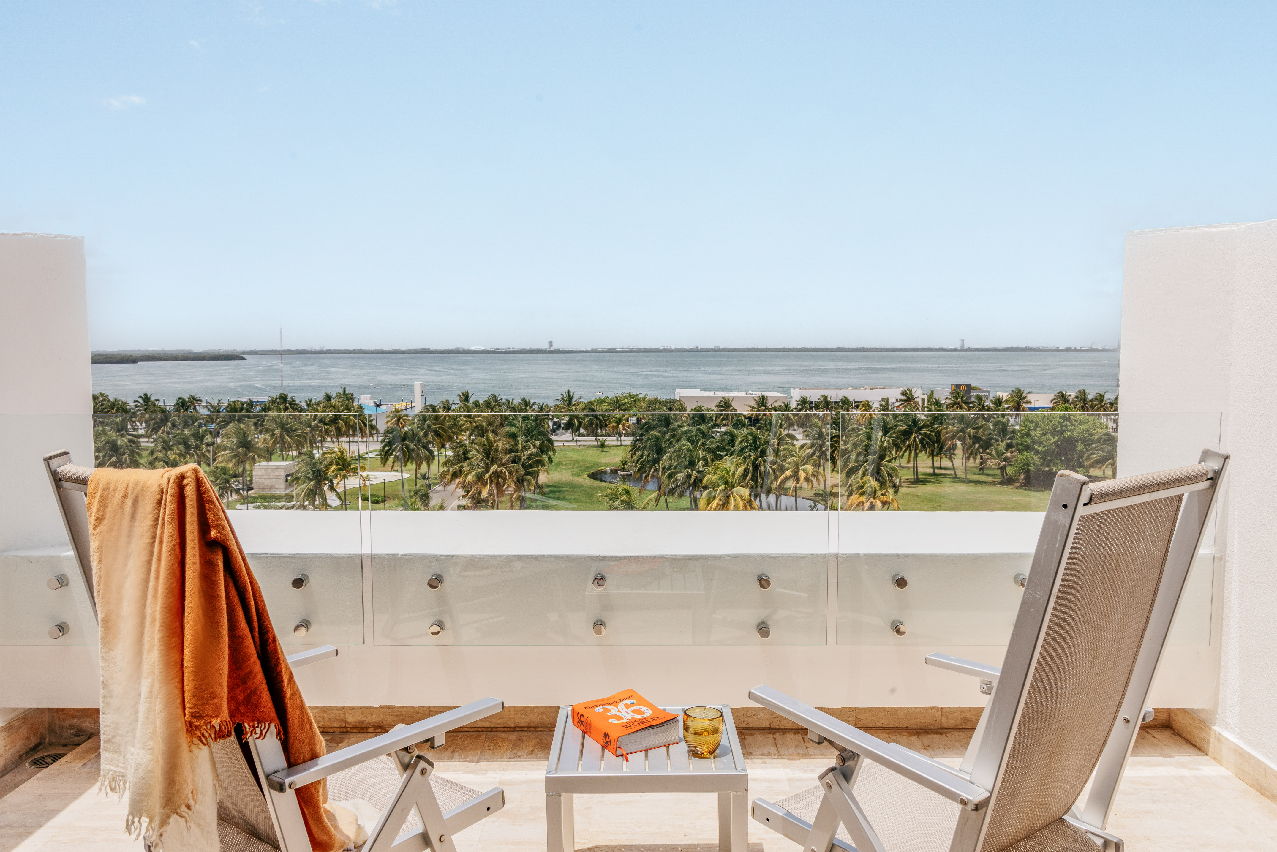 Balcony with ocean view, tropical palm trees, lounge chairs, and a book.