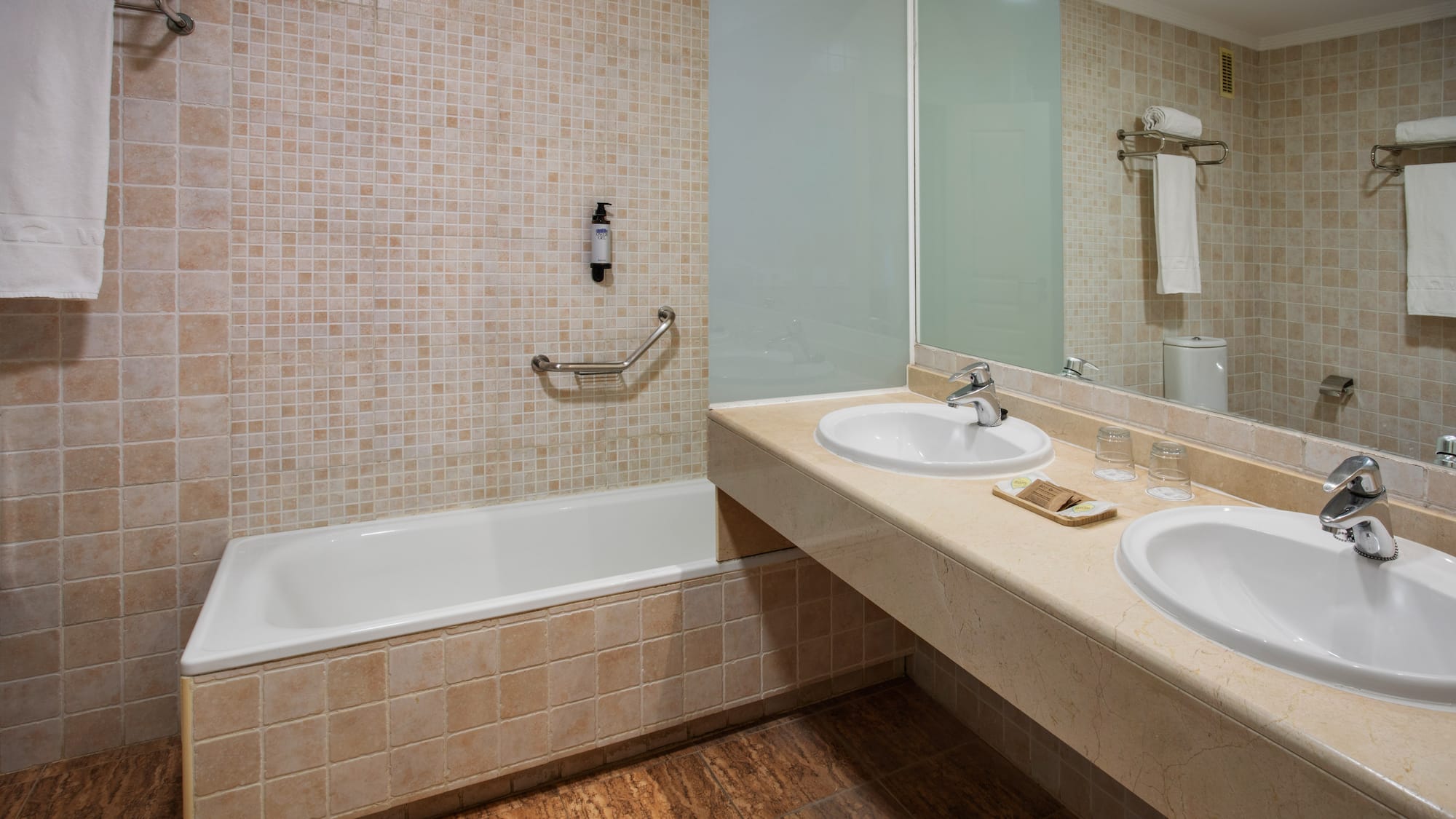 Bathroom with bathtub, double sink vanity, beige tiled walls and floor.