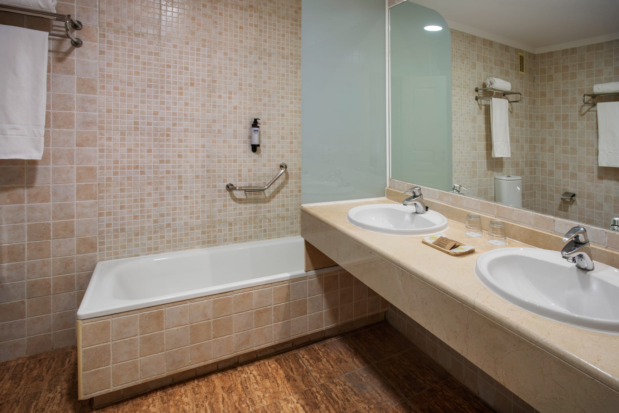 Bathroom with bathtub, double sink vanity, beige tiled walls and floor.