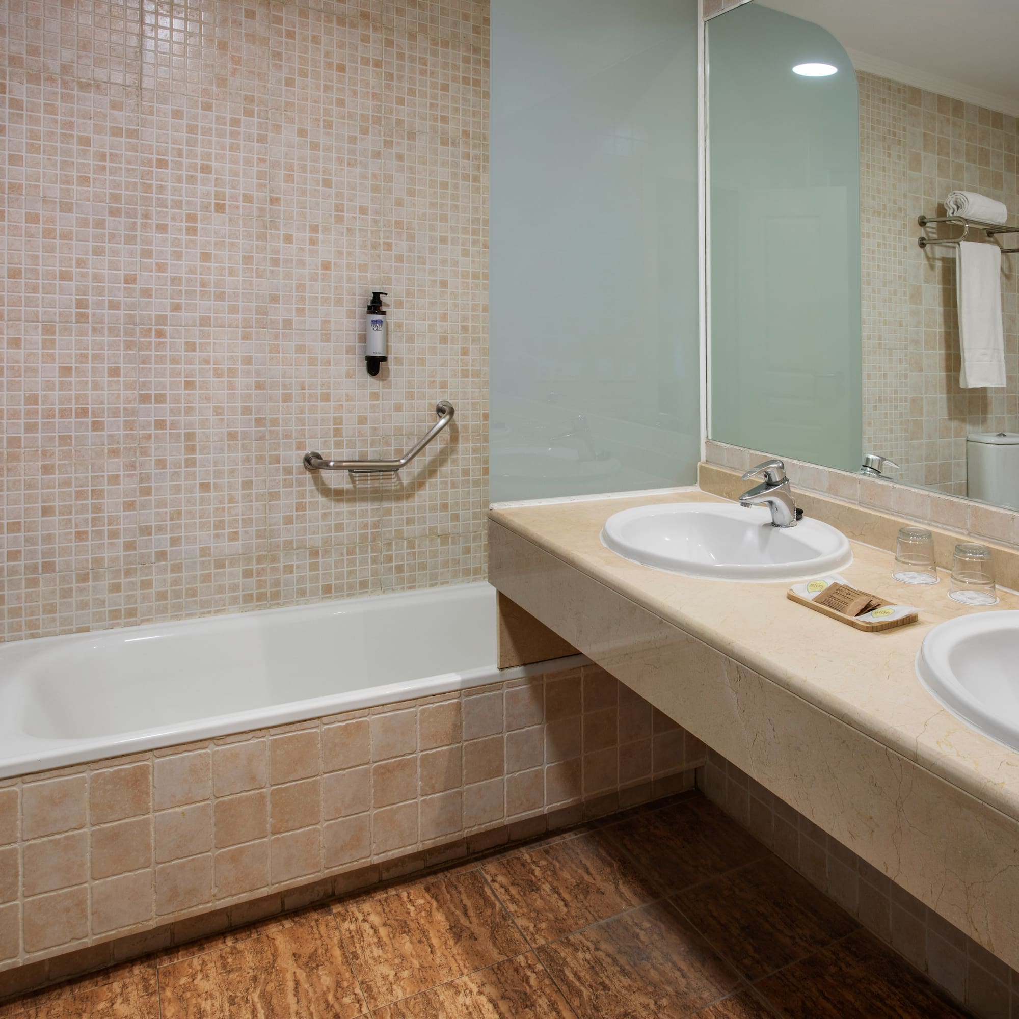 Hotel bathroom with bathtub, double vanity, mirror, and mosaic tiles.