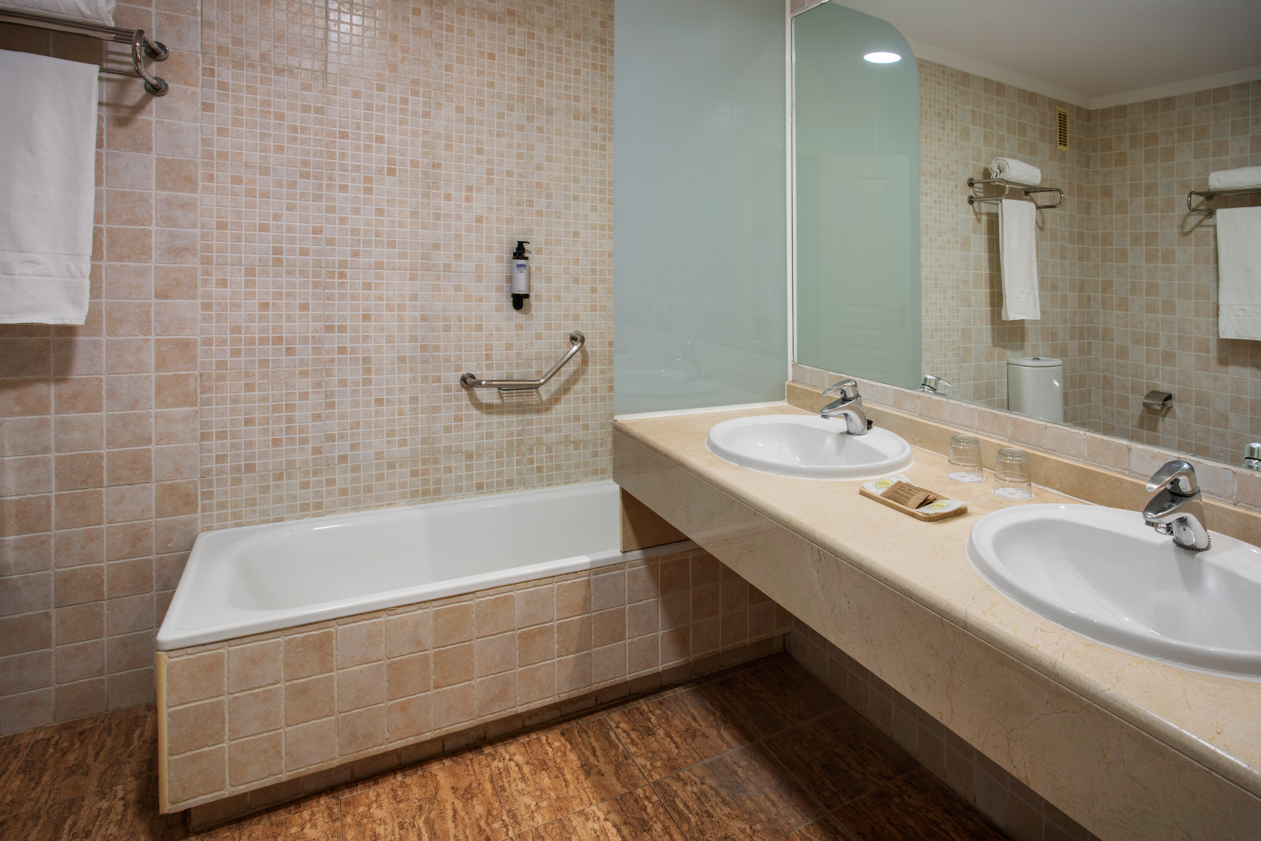 Bathroom with bathtub, double sink vanity, beige tiled walls and floor.