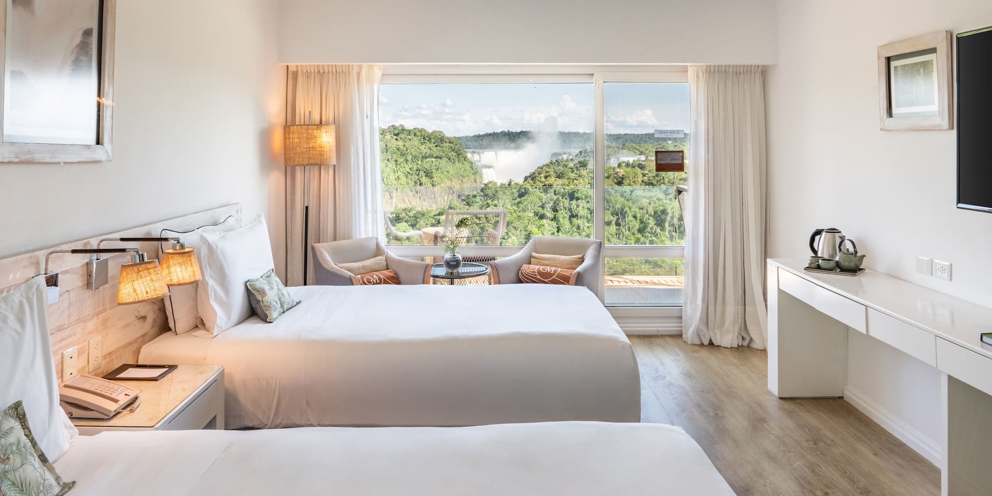 a room with two beds and a table with a view of the mountains