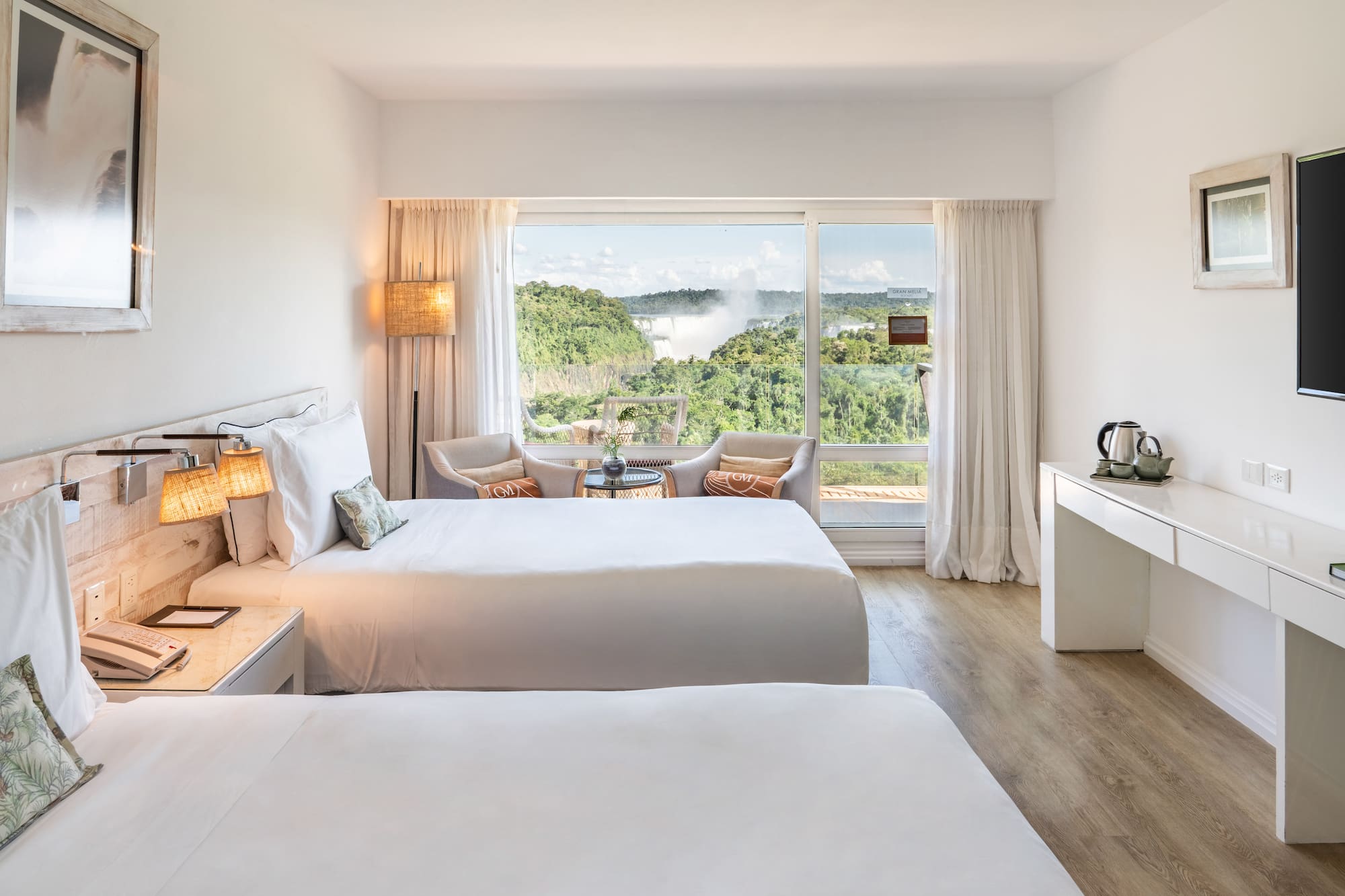 a room with two beds and a table with a view of the mountains