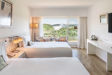 a room with two beds and a table with a view of the mountains