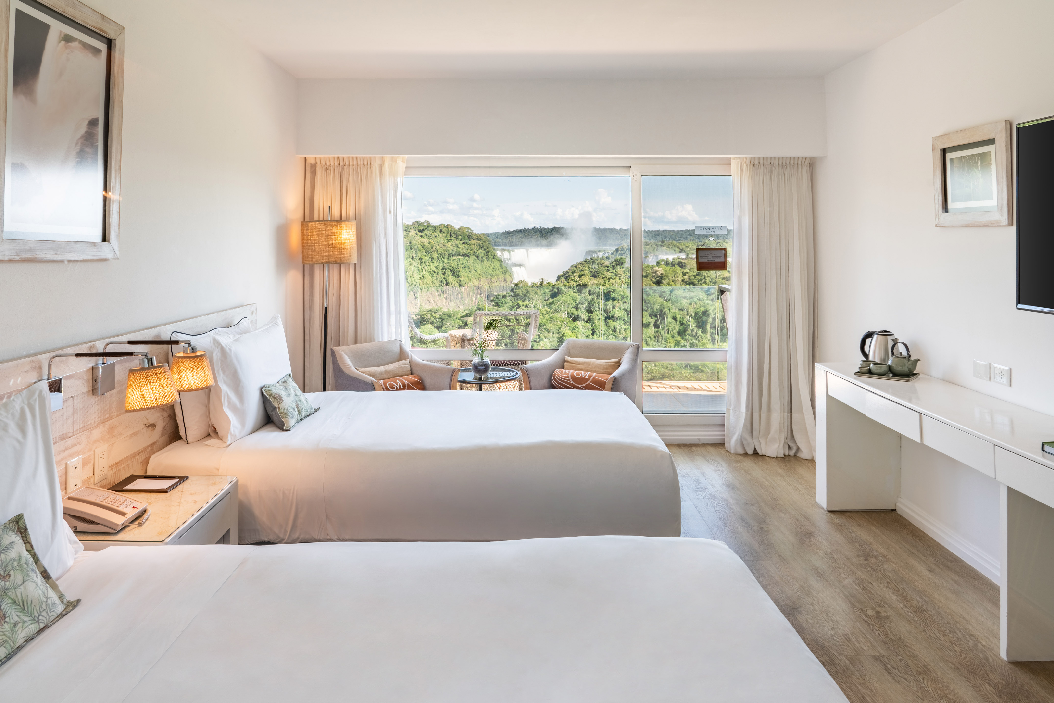Hotel room with twin beds and a stunning view of Iguazu Falls and lush rainforest.