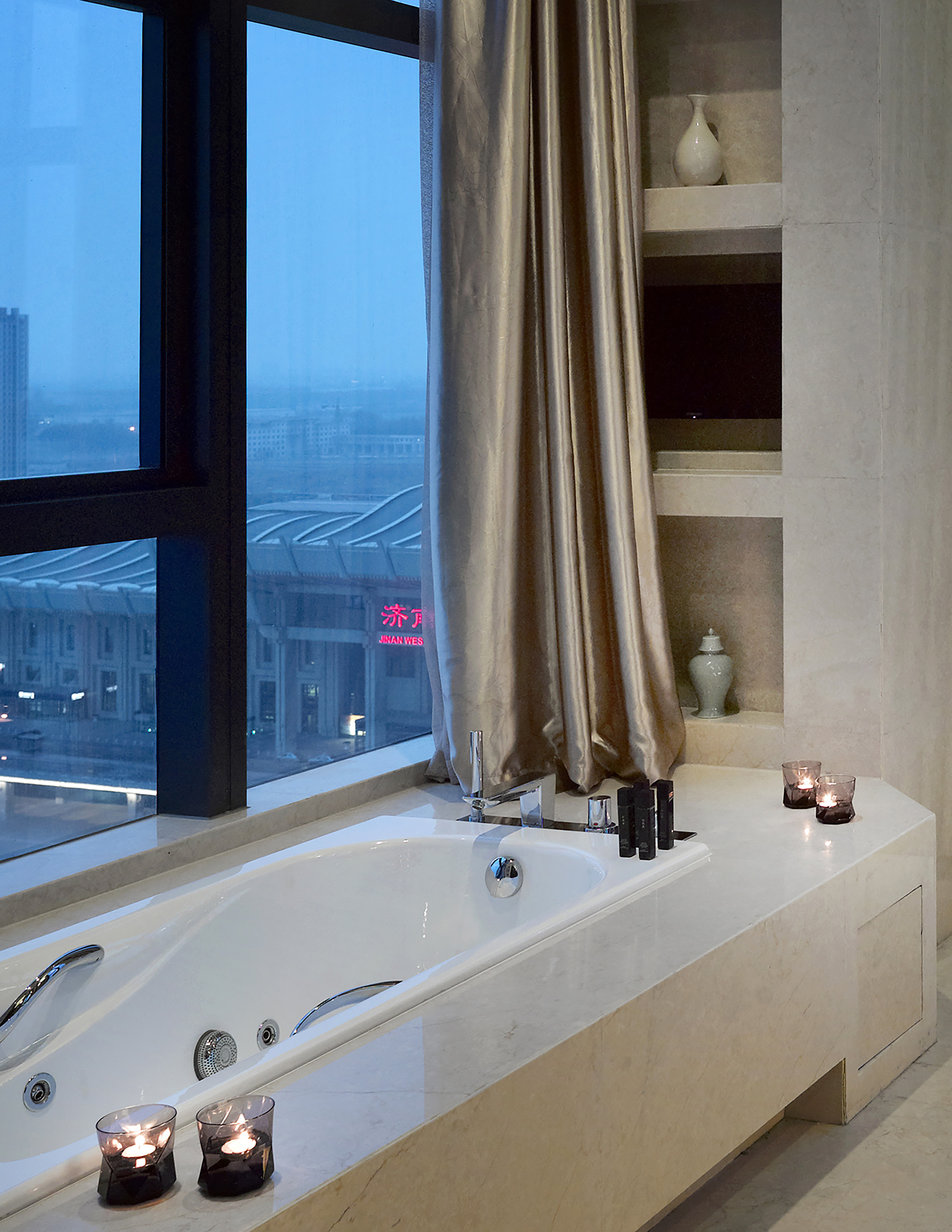 Modern luxury bathtub with city view, ambient candles, and marble accents.
