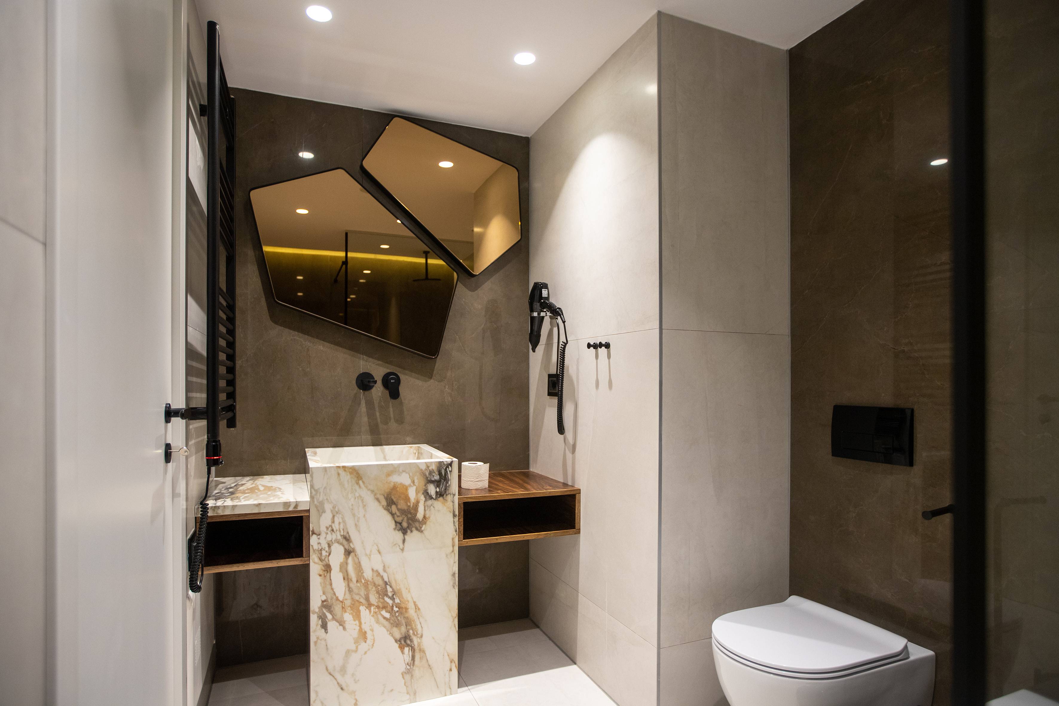 Modern bathroom with marble vanity, geometric mirrors, and dark fixtures.