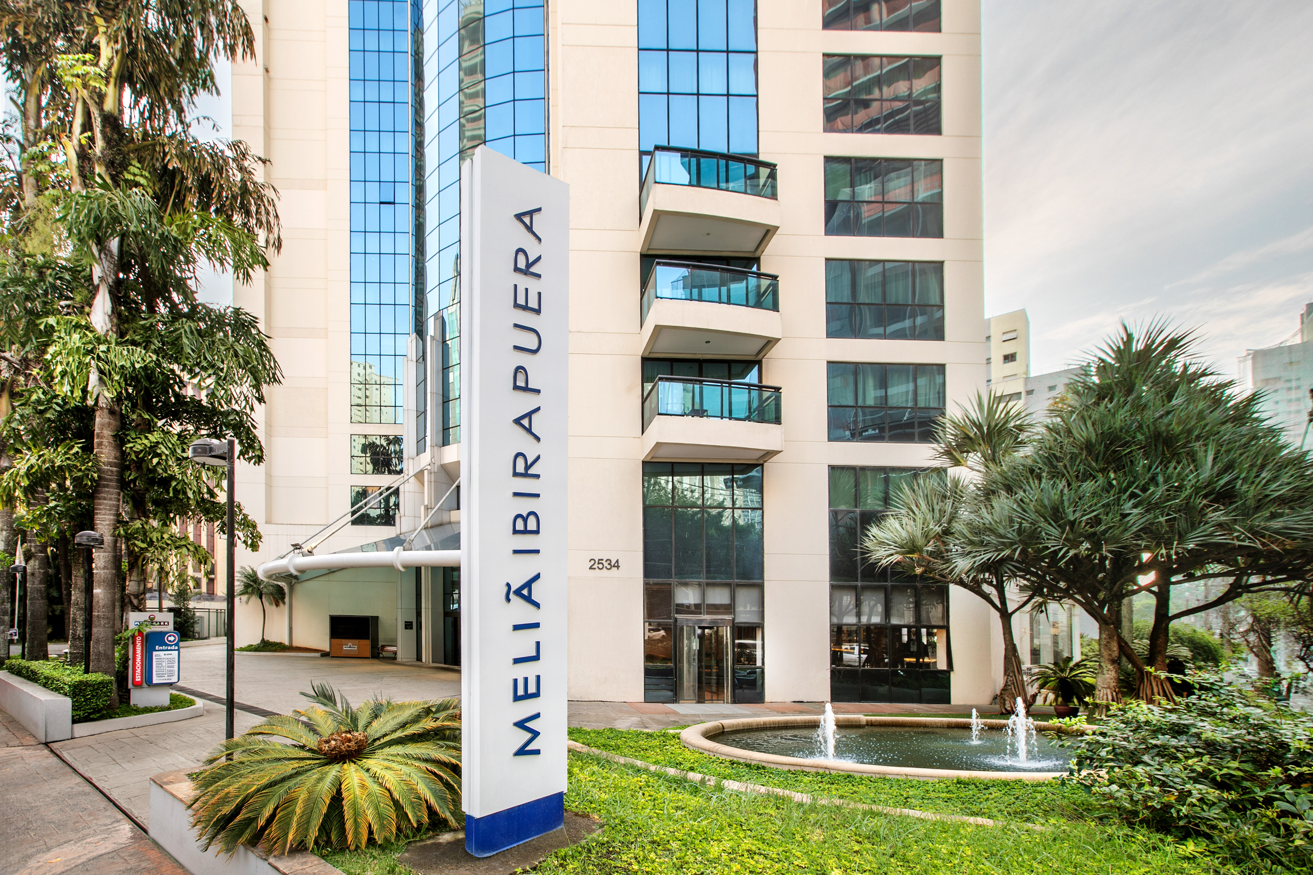 Fachada del hotel Meliá Ibirapuera con un cartel blanco, fuentes y vegetación. - Meliá Ibirapuera, Sao Paulo
