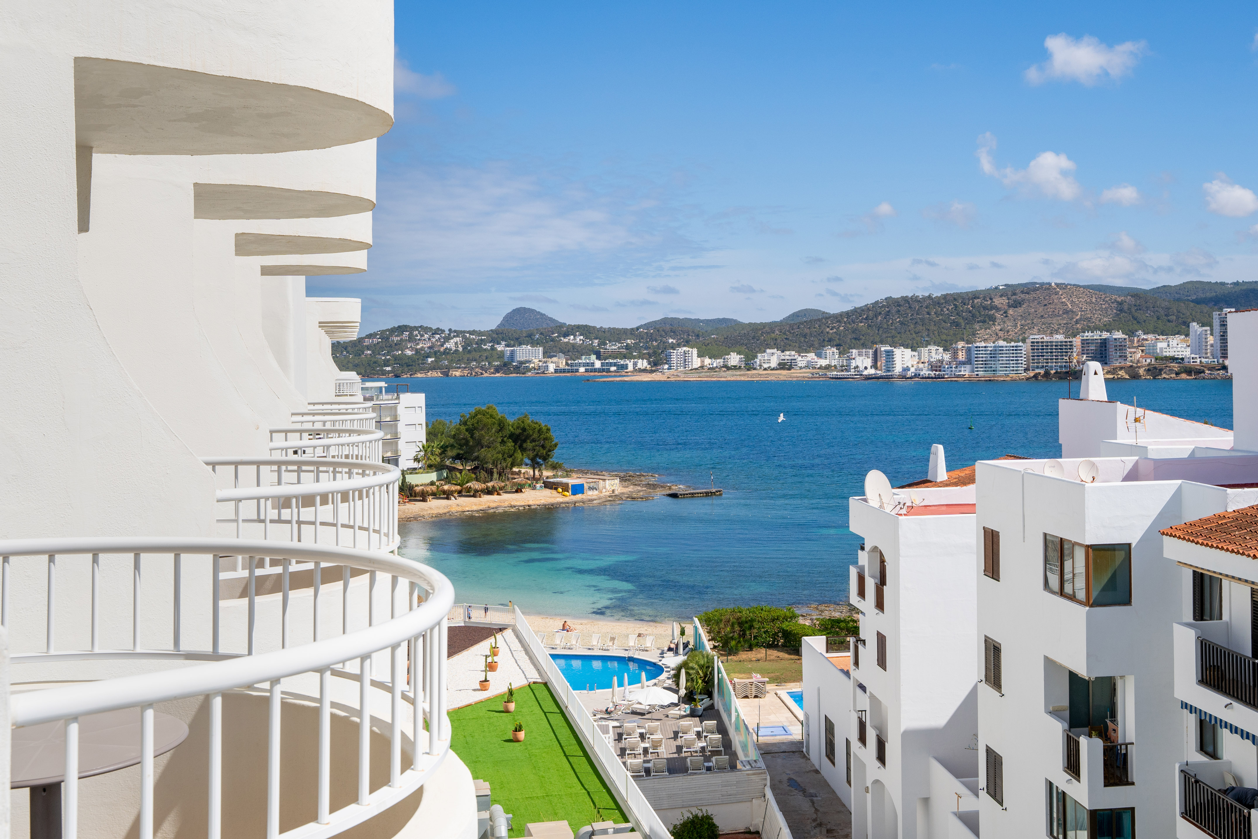 Hotel balconies with sea view, beach, swimming pool, and coastal town.