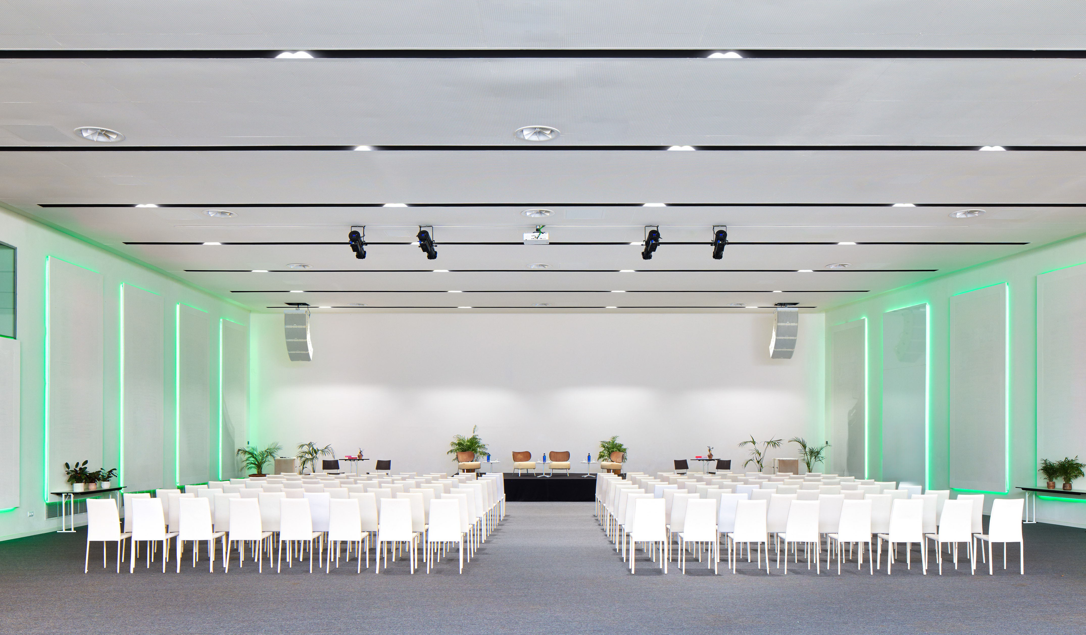 Modern conference room with white chairs, stage, and vibrant green wall lighting.