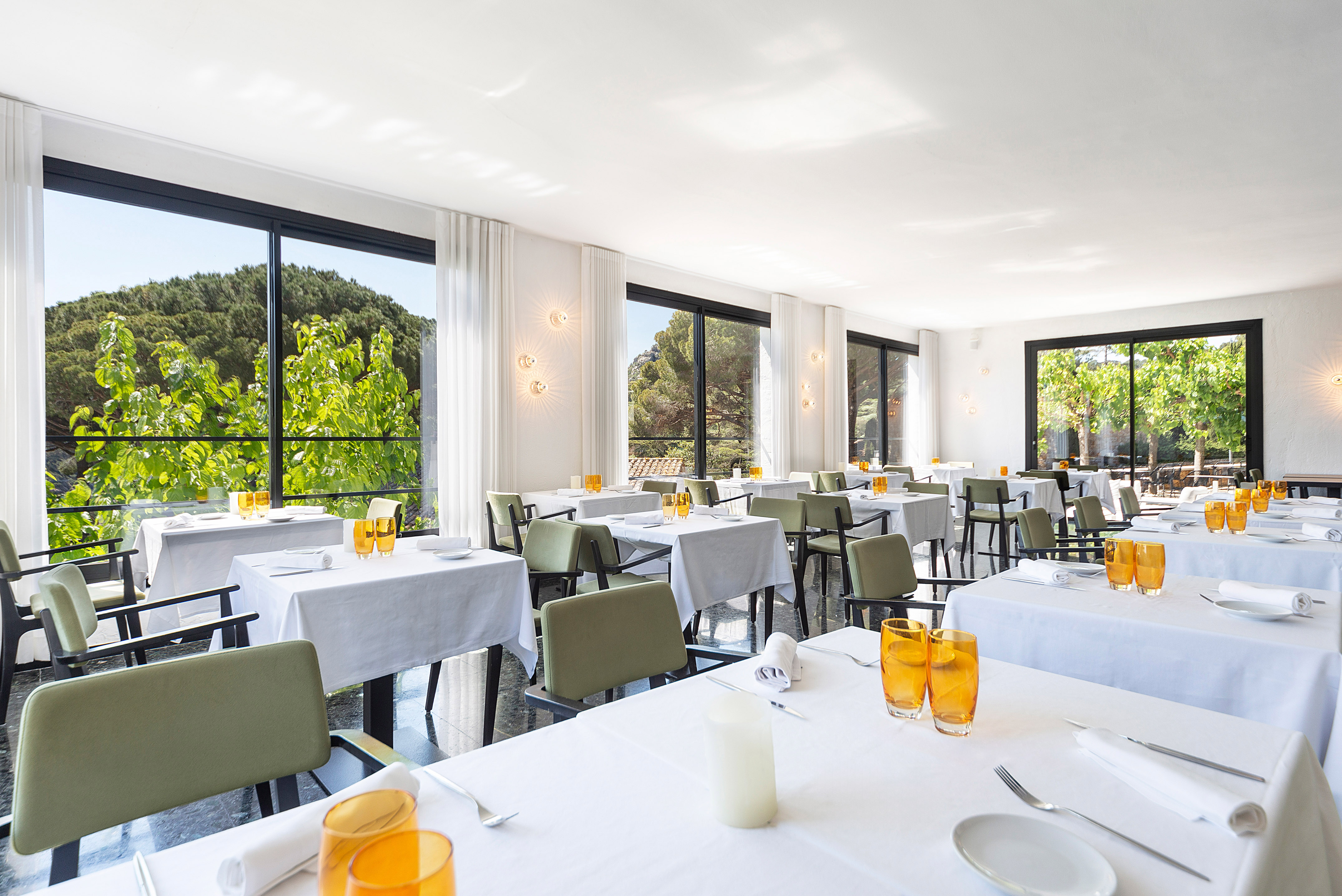 Bright restaurant dining room with white tables, green chairs, and scenic green views.