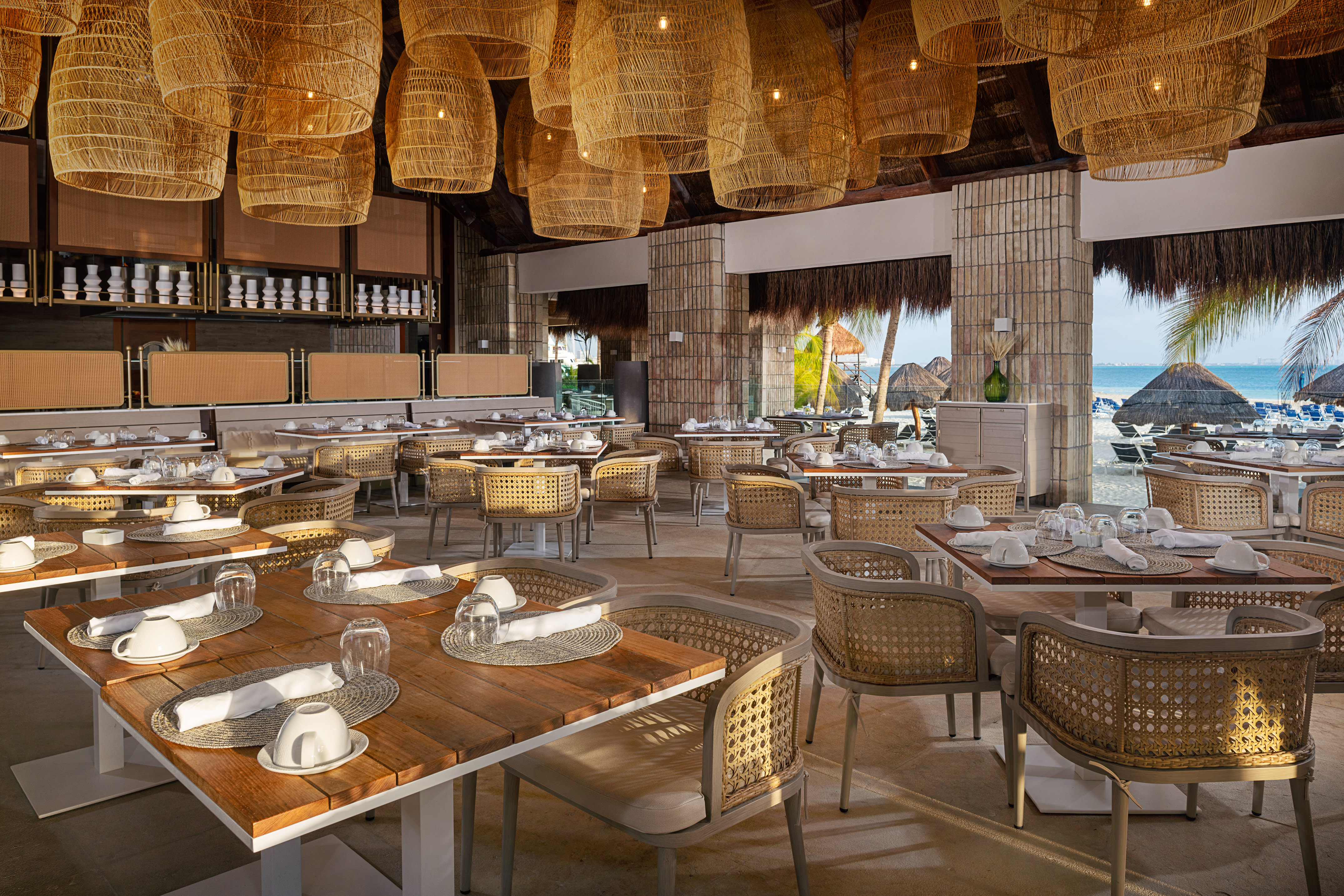 Tropical beachfront restaurant with rattan chairs, wooden tables, and ocean view.