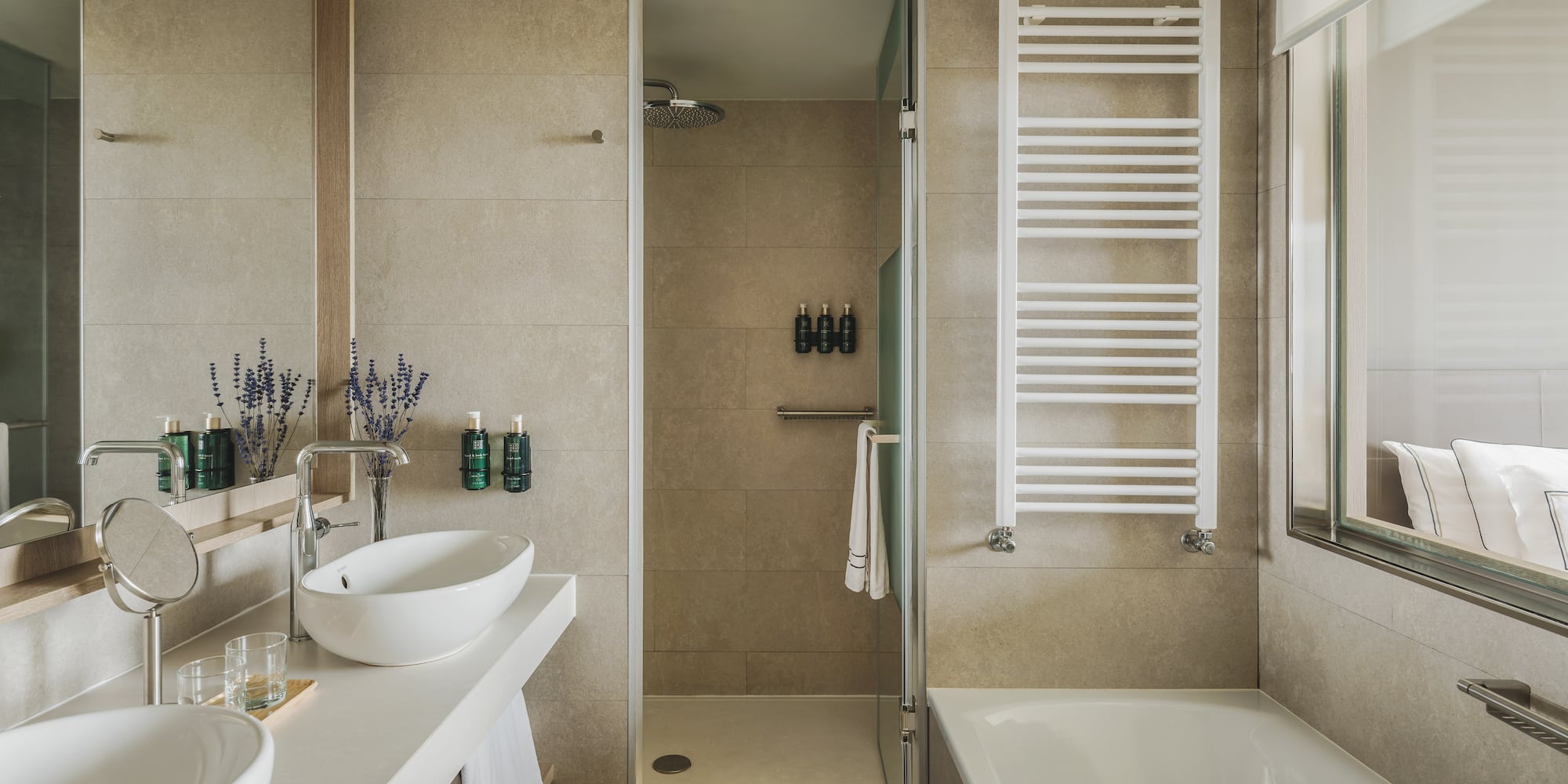 Baño moderno de hotel con doble lavabo, ducha, bañera y toallero.