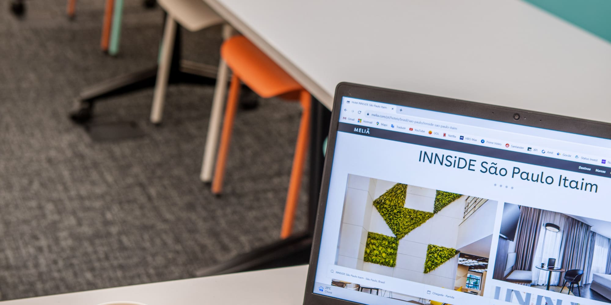 a laptop on a table with a cup of coffee and a long table with chairs