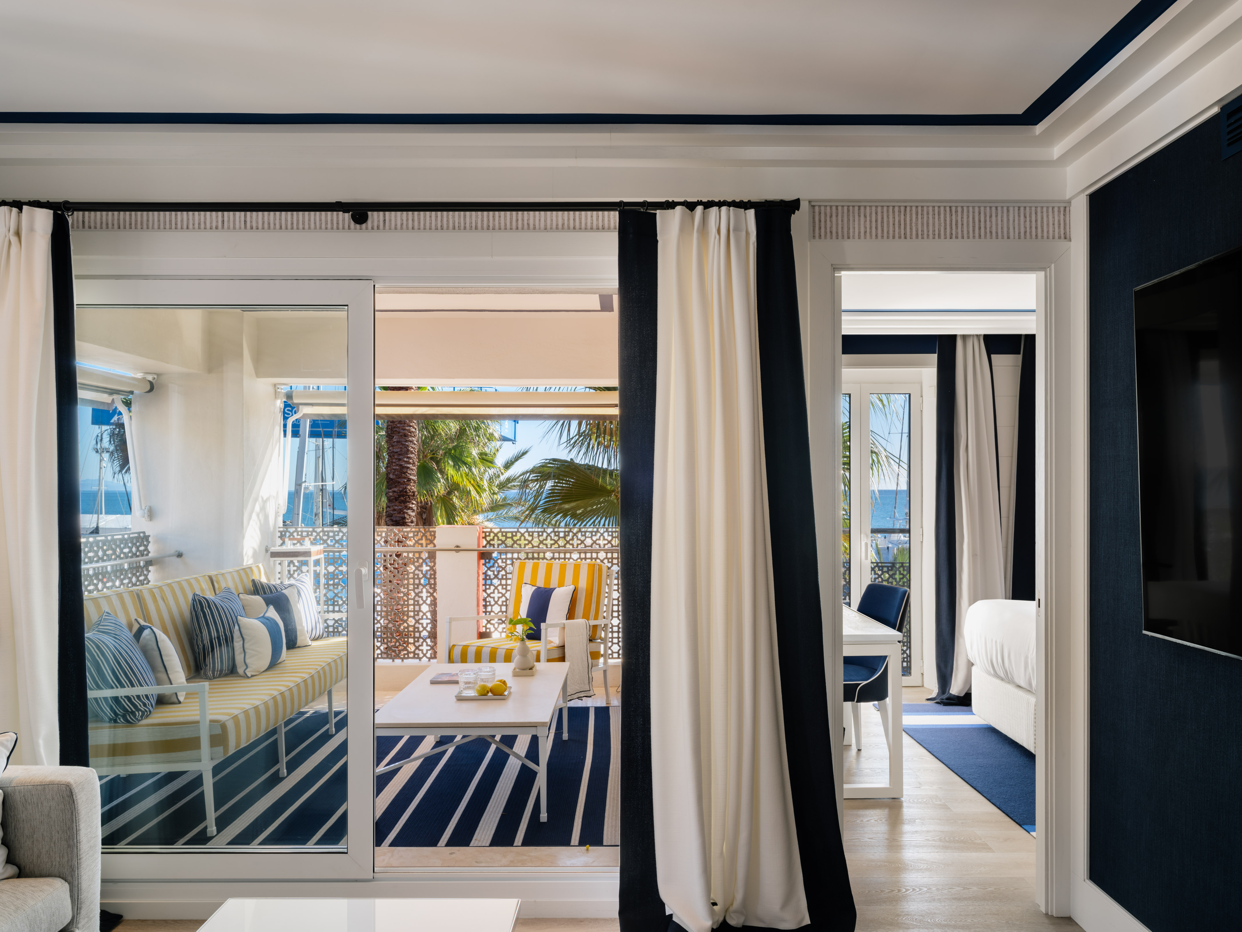 Luxury hotel suite with ocean view balcony and blue & white coastal decor.