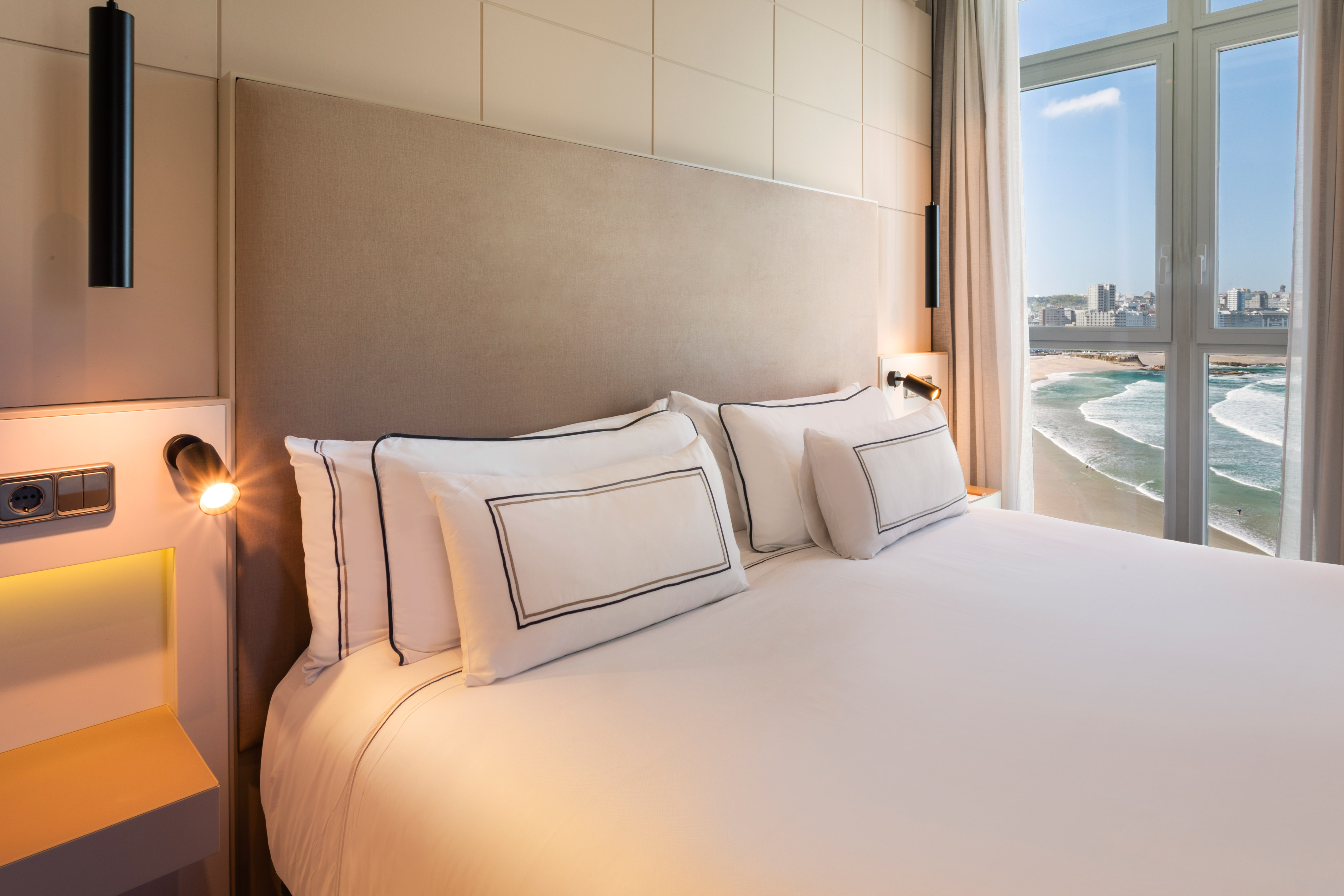Hotel bedroom with sea view, white bed, and modern decor.