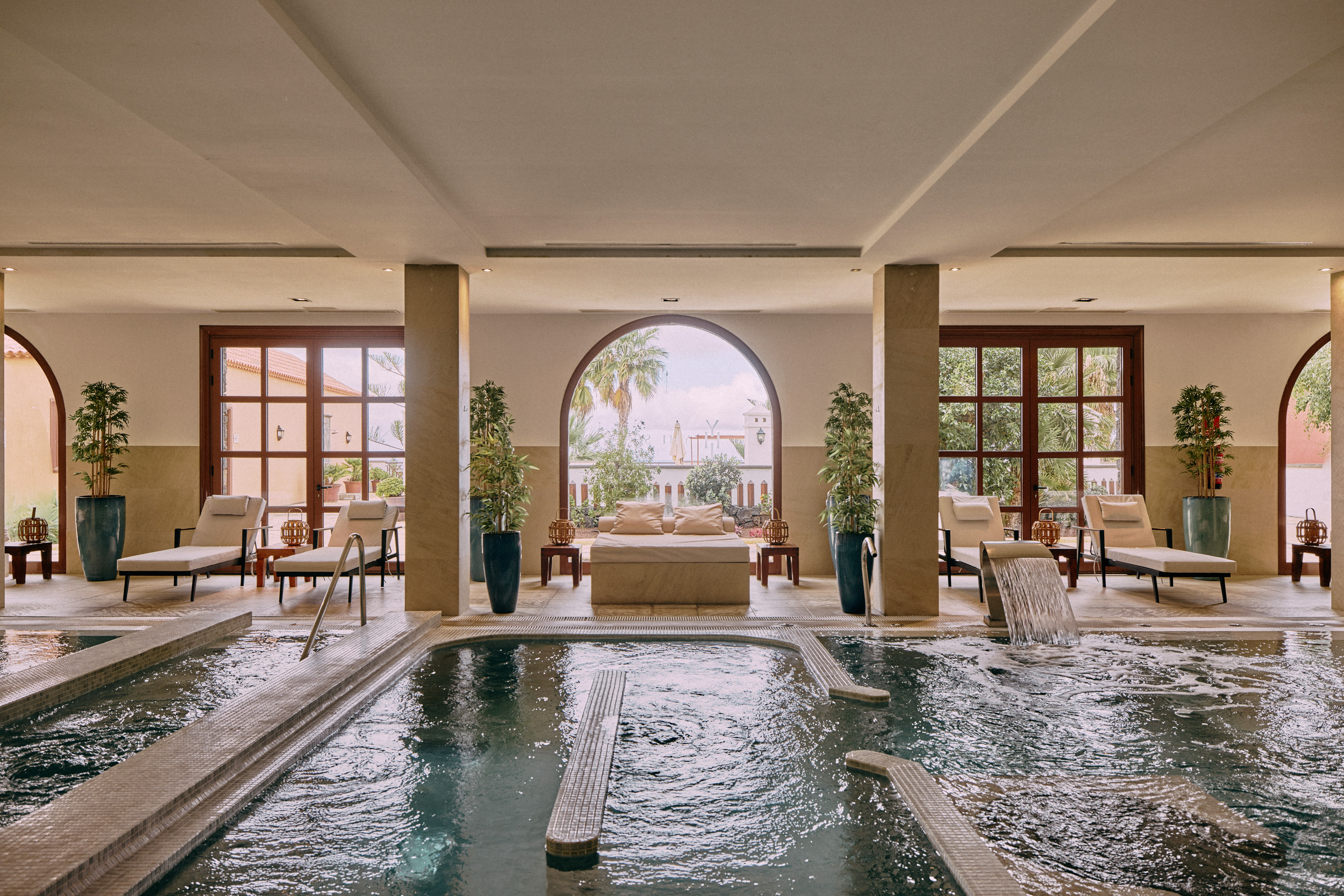 Elegant indoor spa: hydrotherapy pool, loungers, archways overlooking garden.