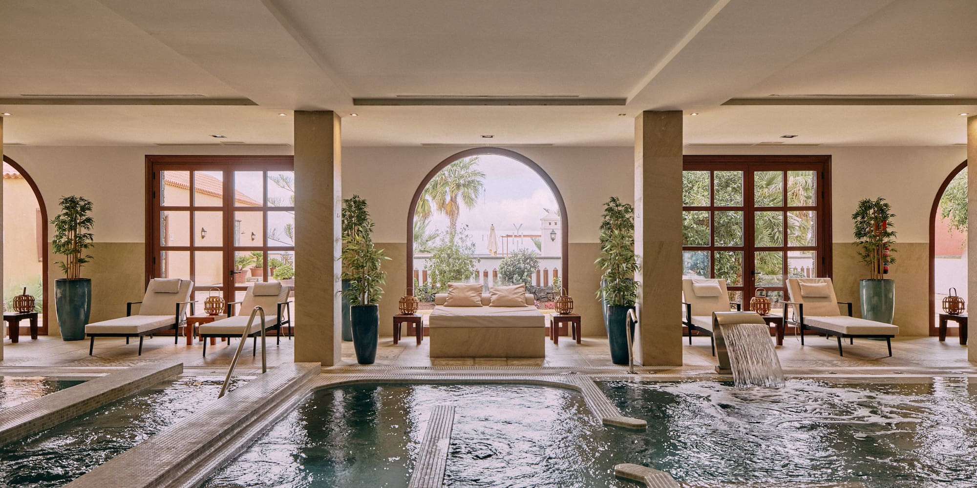 Elegant indoor spa: hydrotherapy pool, loungers, archways overlooking garden.