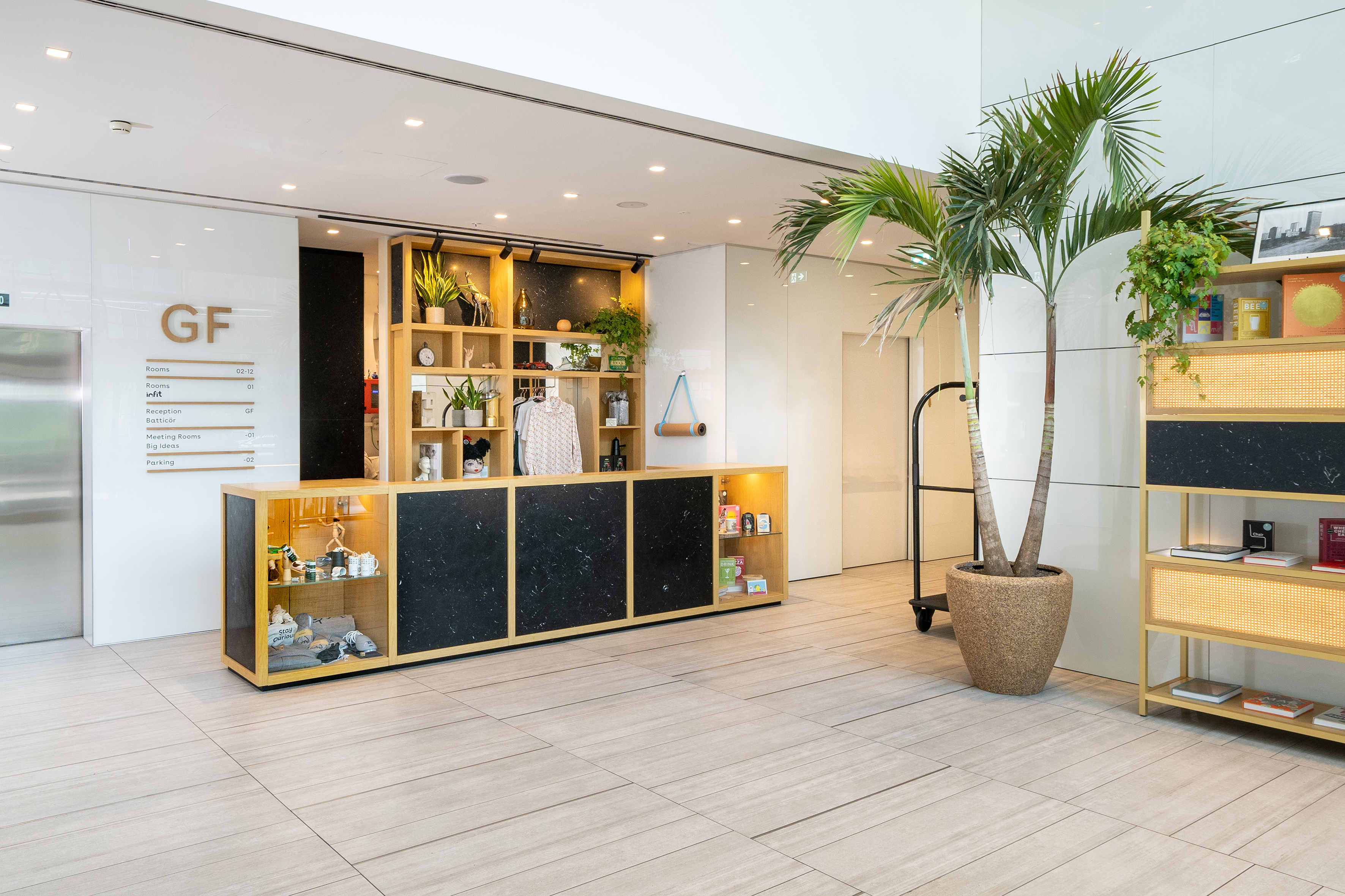 Hotel lobby with modern reception desk, retail display, plants, and directory.