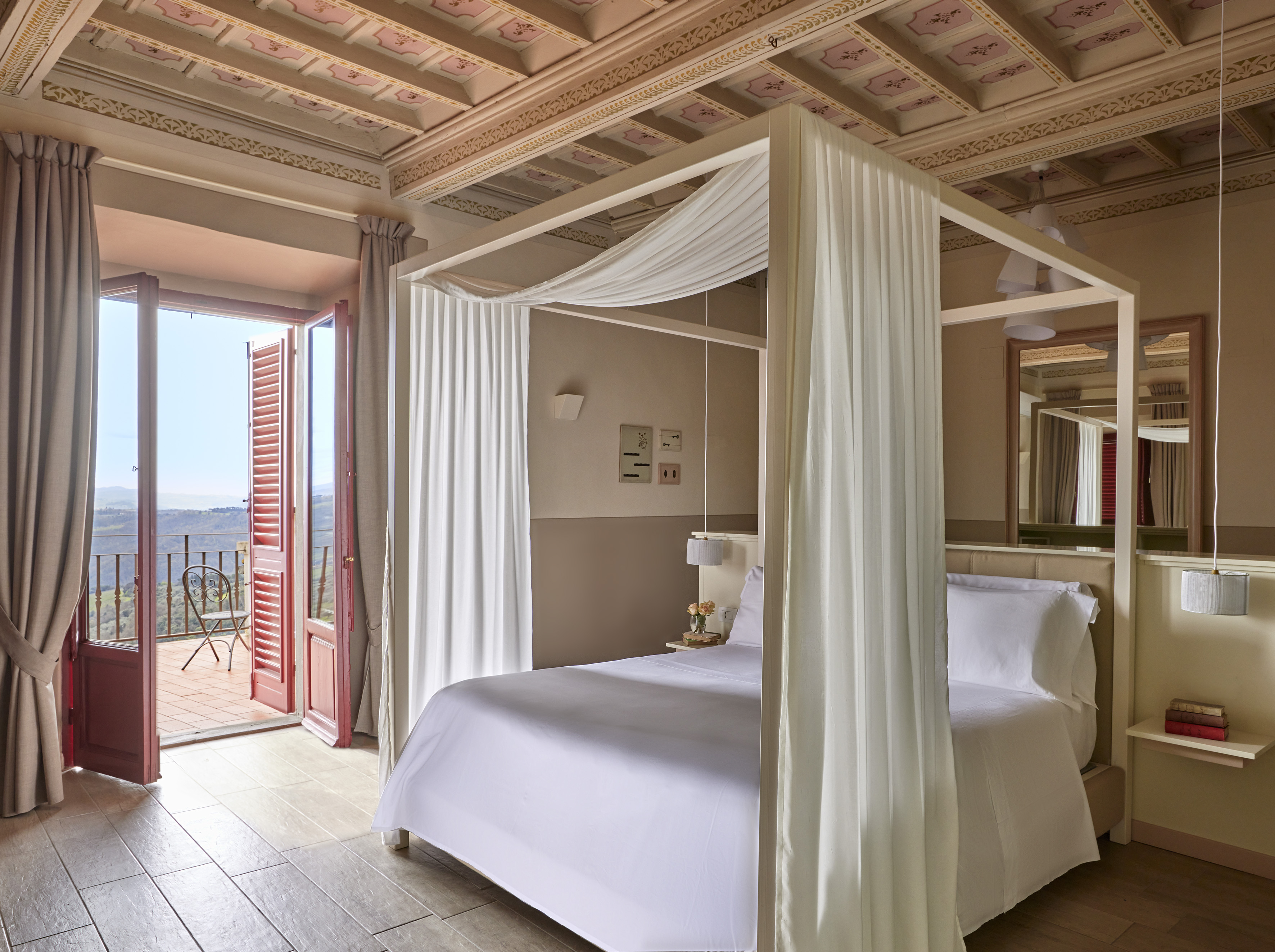 Four-poster bed, ornate ceiling, hotel balcony with scenic mountain view.