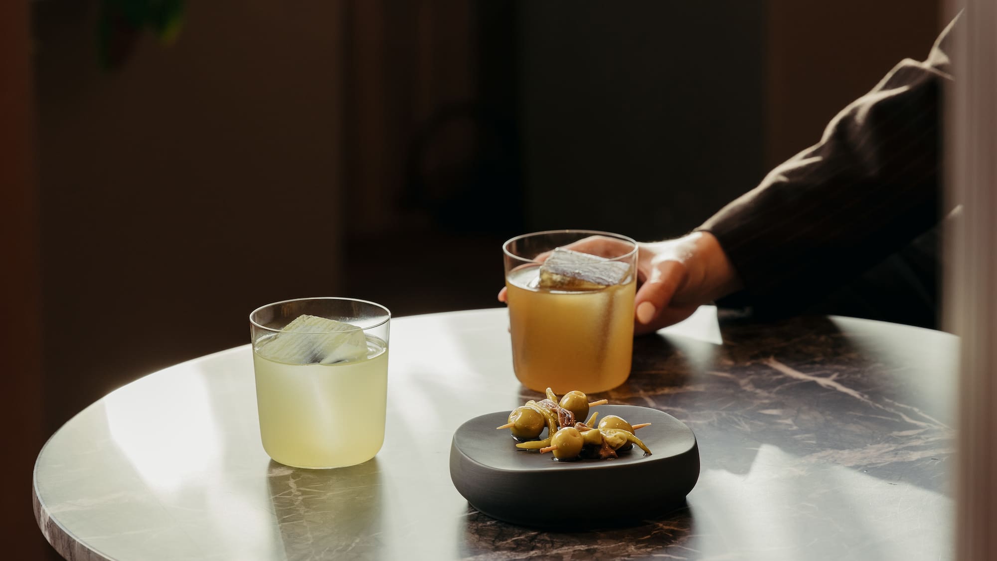 a person holding a drink and a plate of food on a table