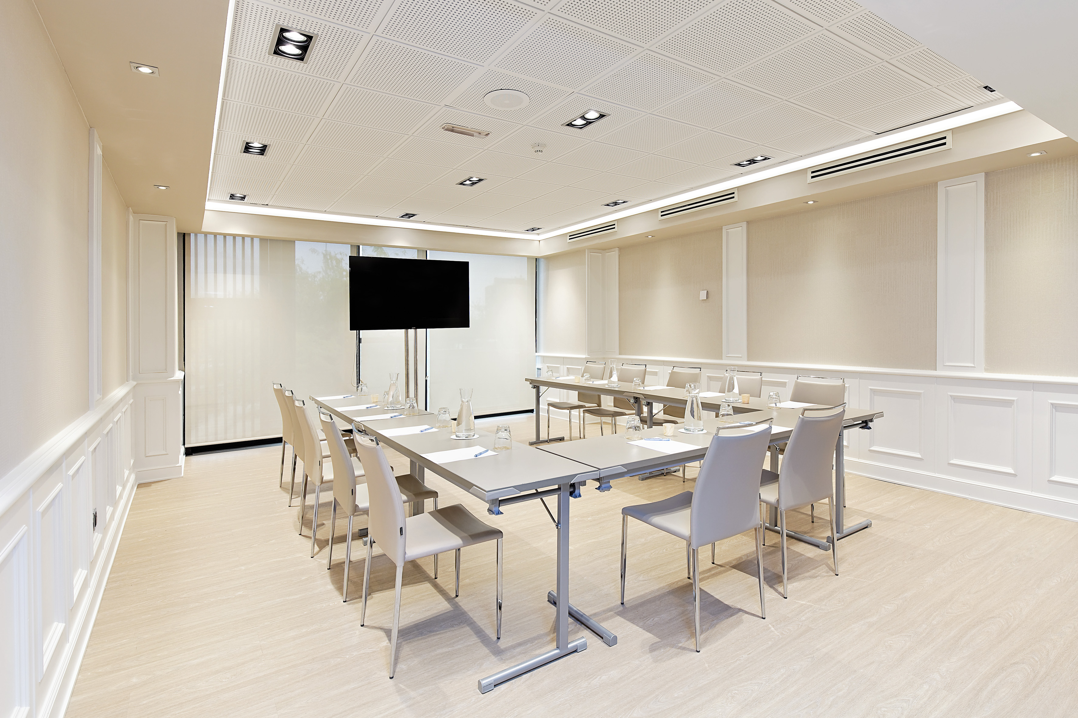 Modern conference room with U-shape table setup, chairs, and presentation screen.