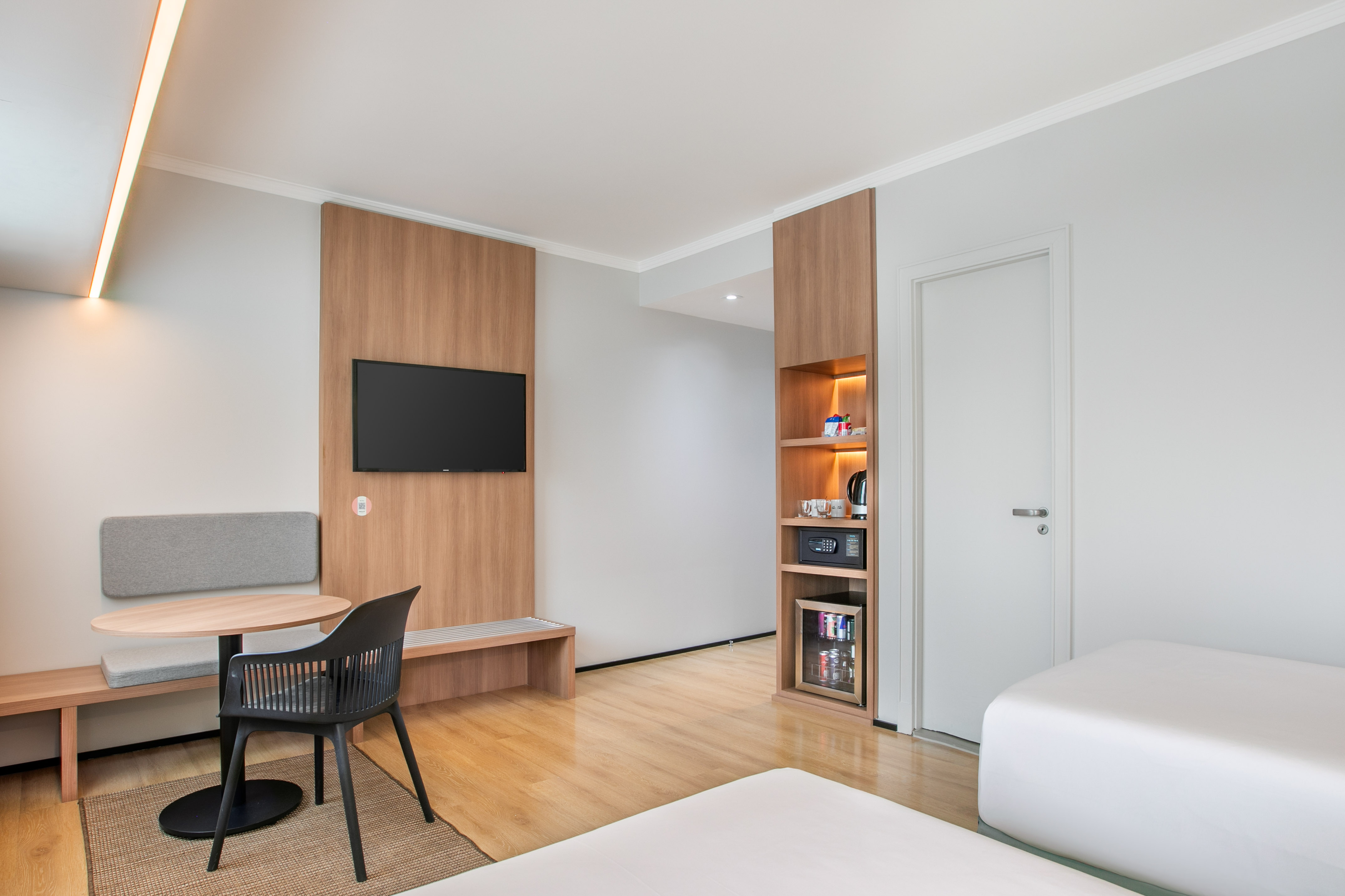 Contemporary hotel guest room with TV, workspace, and minibar cabinet.